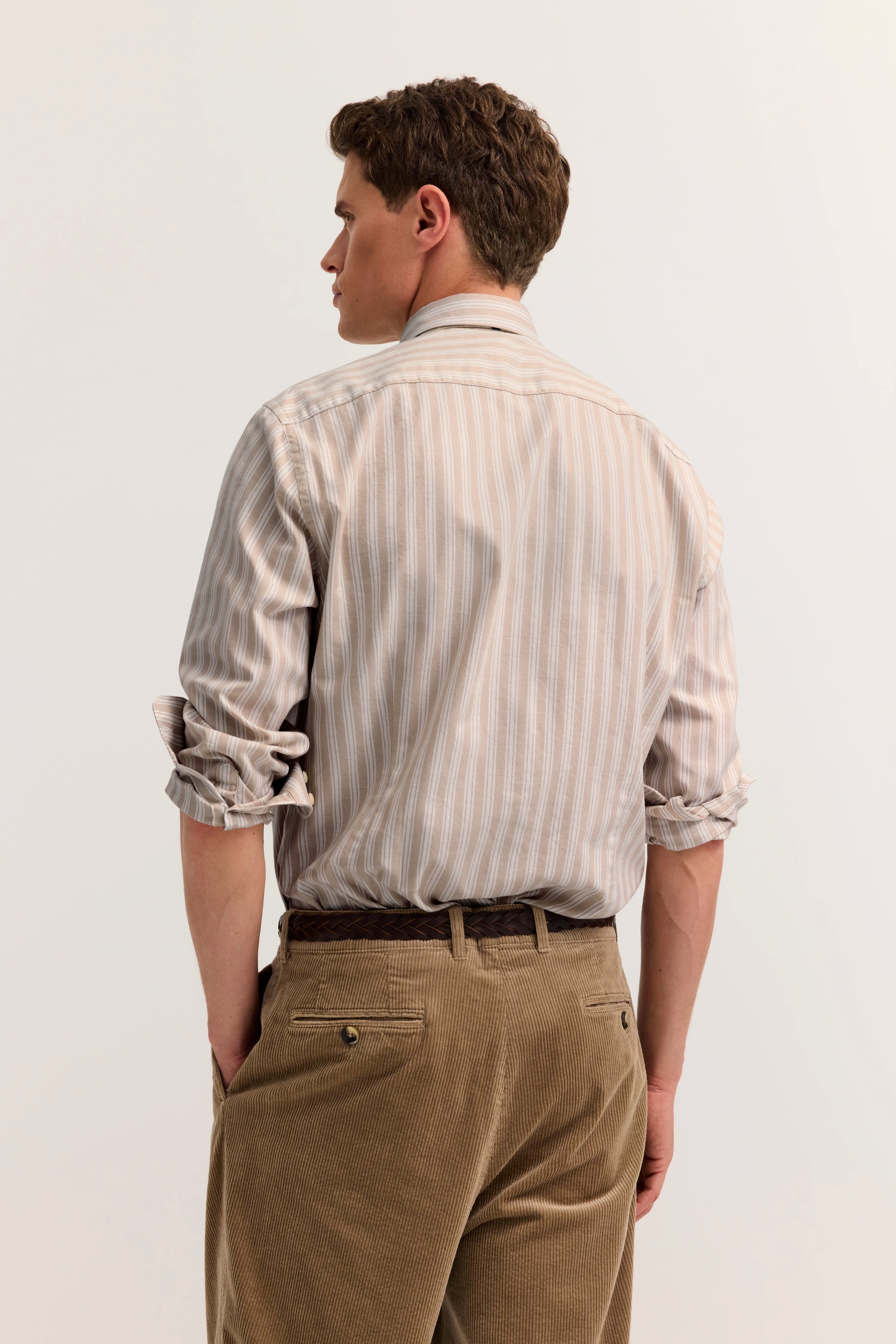Gestreiftes Hemd in Beige und Khaki, lässig hochgekrempelt, von hinten gesehen, Model mit entspannter Haltung.