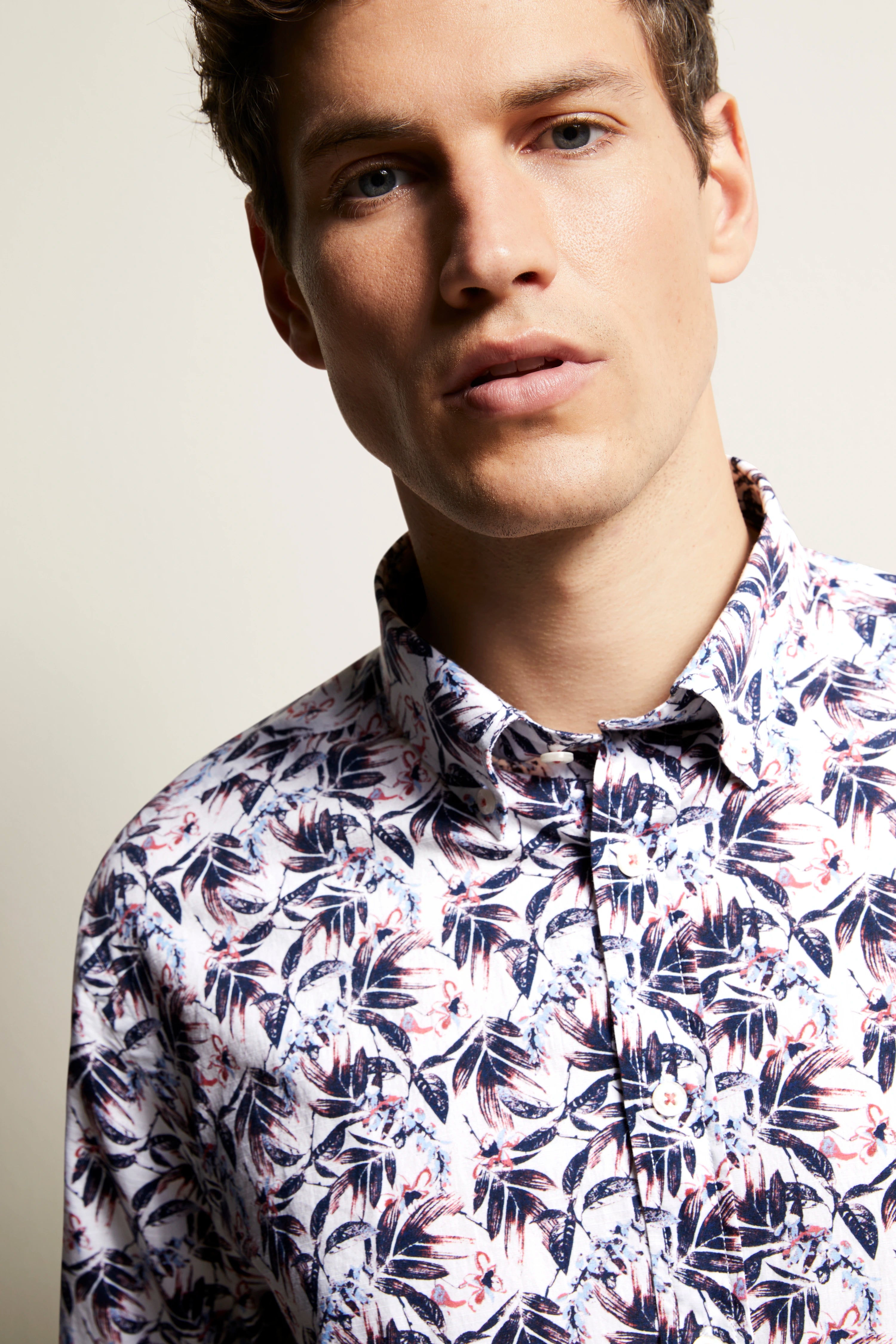Model draagt een wit, blauw en rood bloemenhemd van bugatti, in een ontspannen pose.
