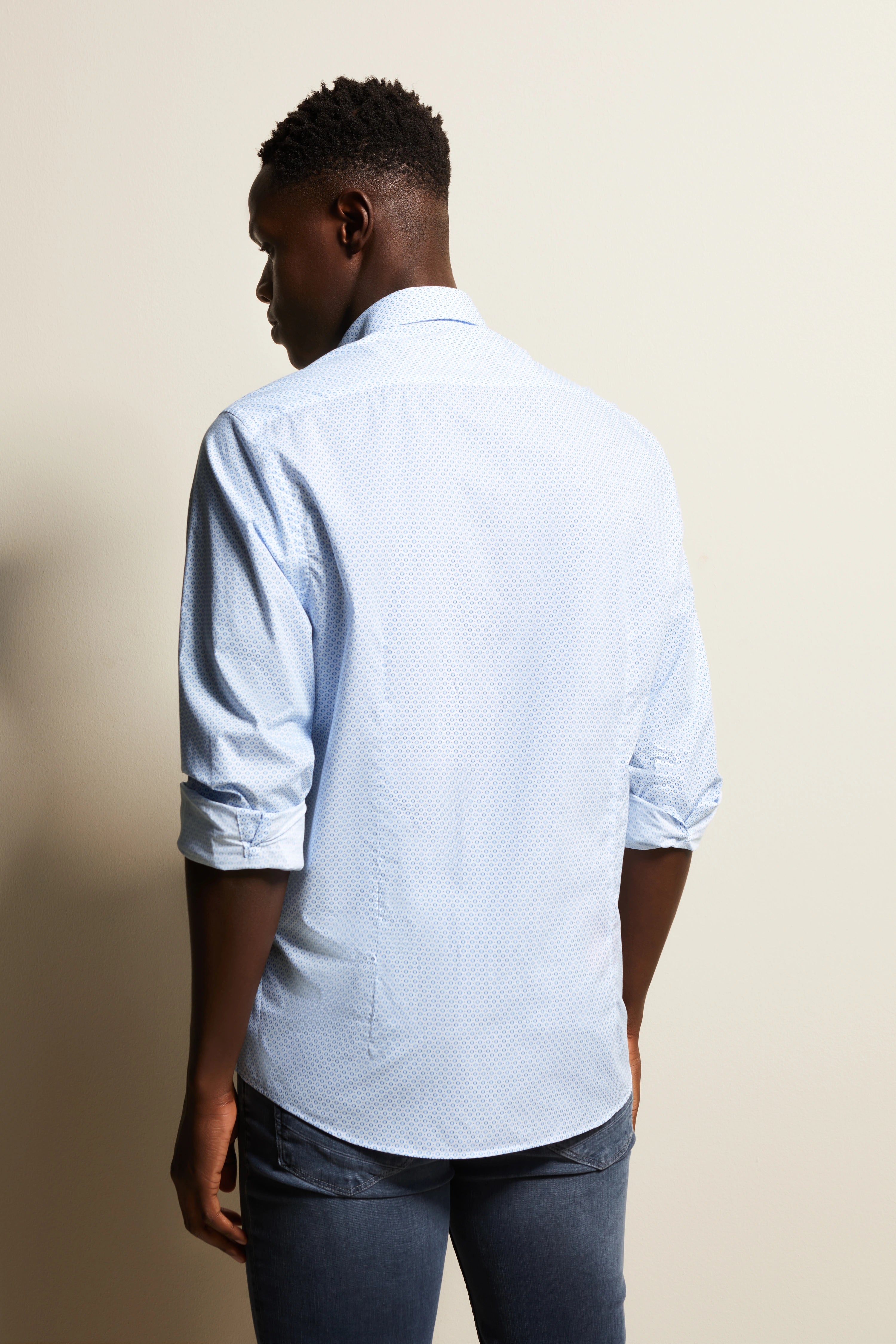 bugatti modelbeeld, lichtblauw overhemd, subtiel patroon, casual jeans, achteraanzicht, ontspannen houding.