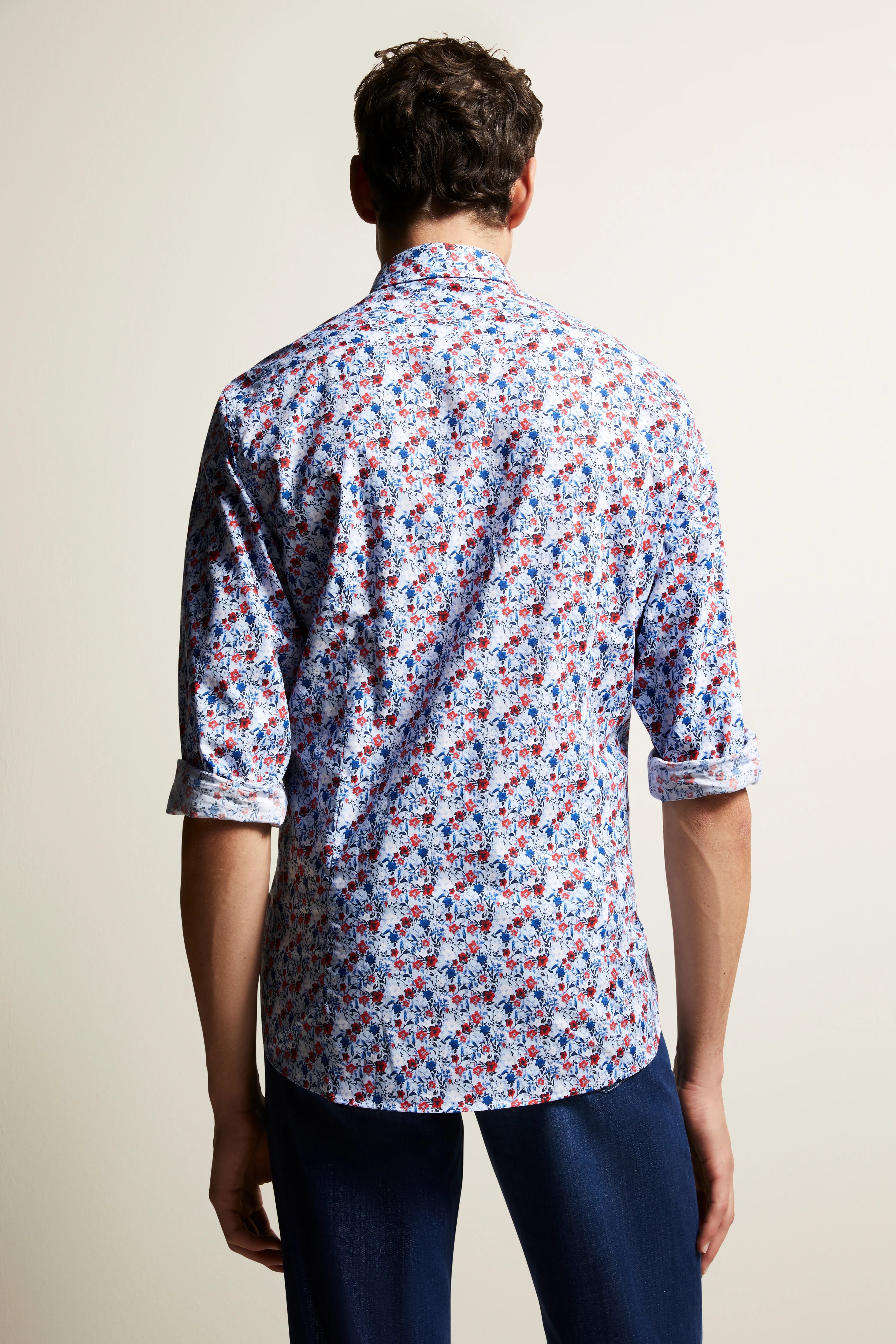 Achterkant van een man in een blauw-rood-wit bloemen bugatti overhemd met nonchalant opgerolde mouwen.