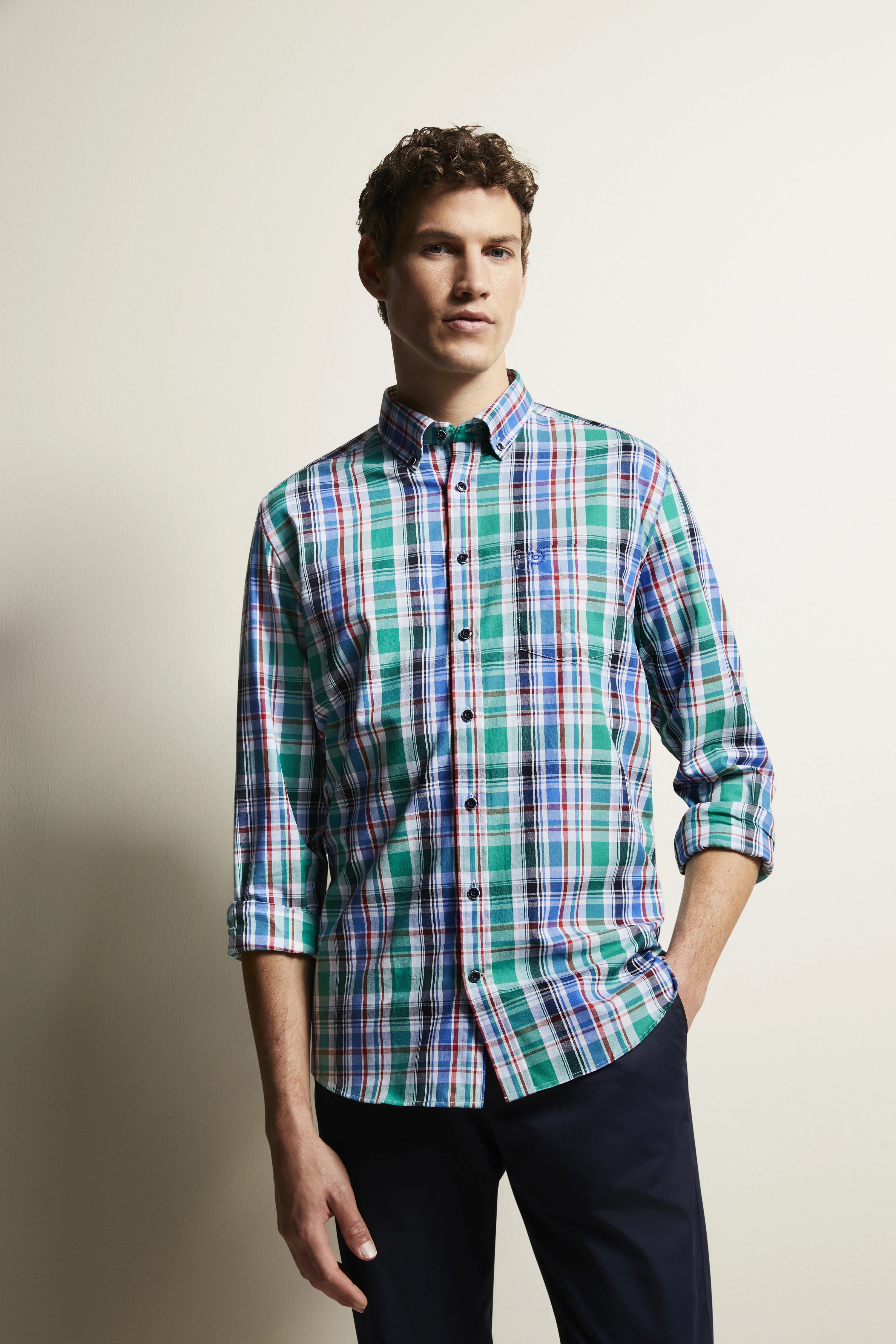 Model in geruit groen-blauw bugatti overhemd, ontspannen pose, zwarte broek.