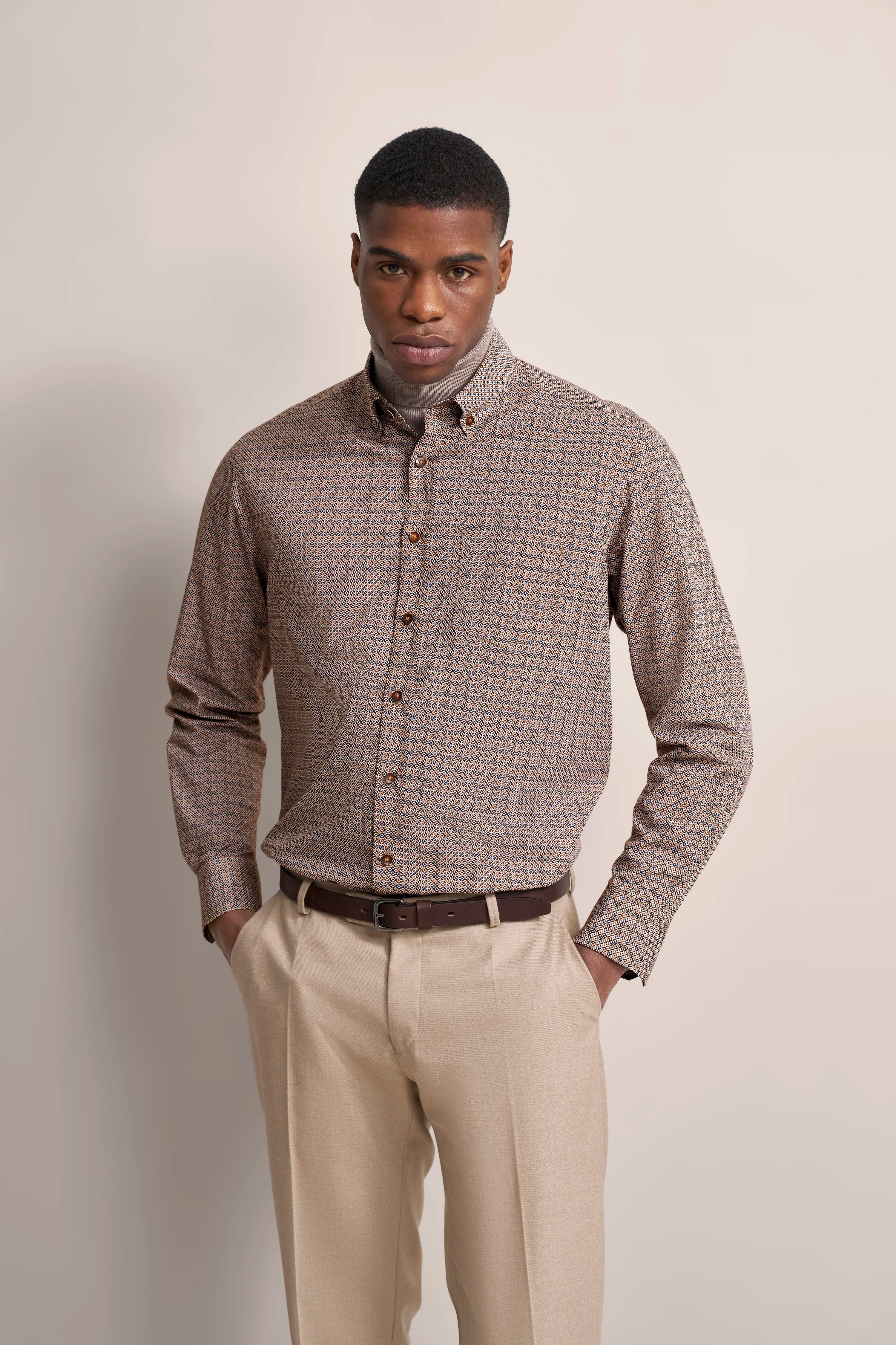 Man in patterned shirt and beige pants by bugatti, model image with relaxed pose.