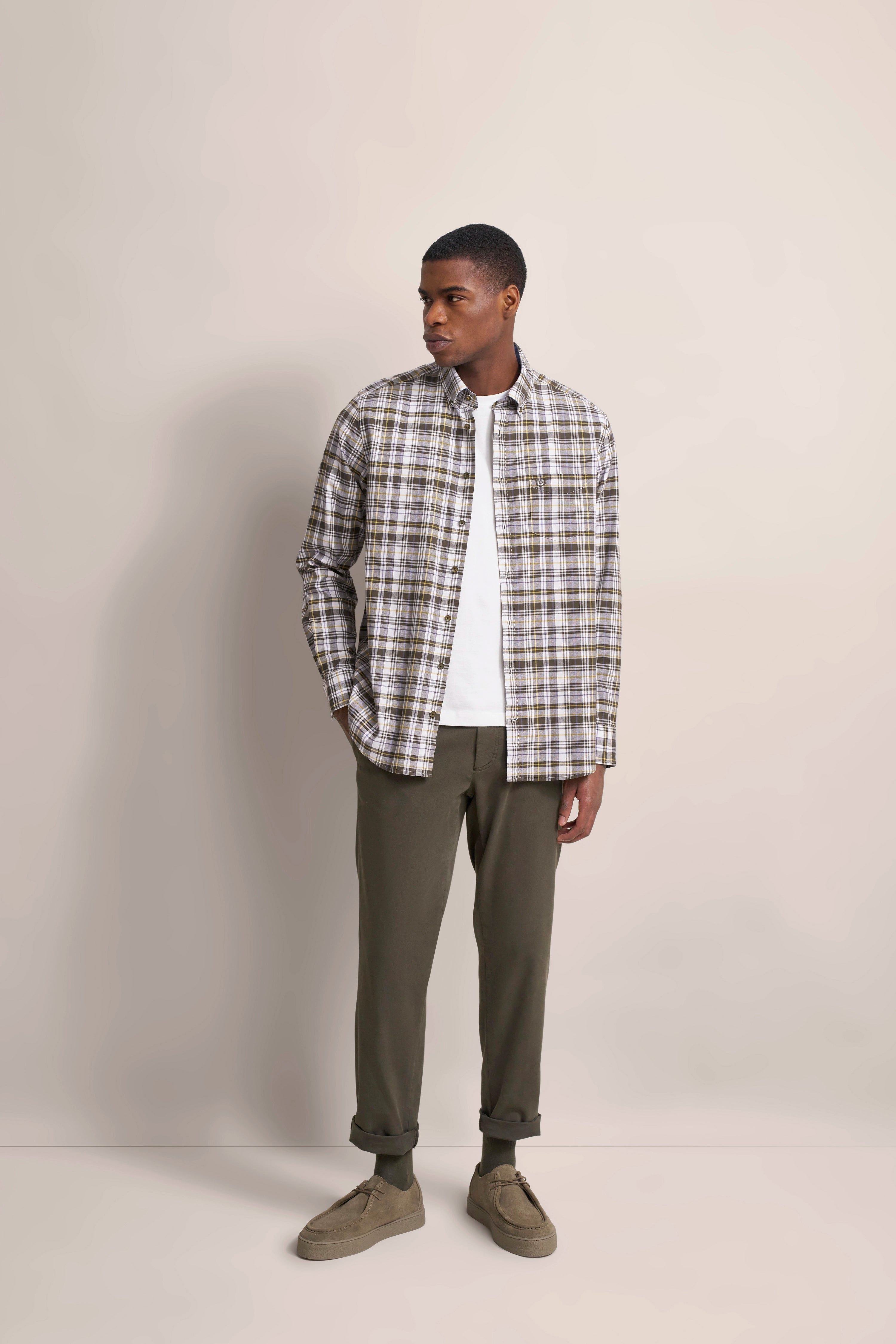 Plaid Hemd in Beige und Grün, weißes T-Shirt, olivgrüne Hose und Schuhe, Model steht lässig.