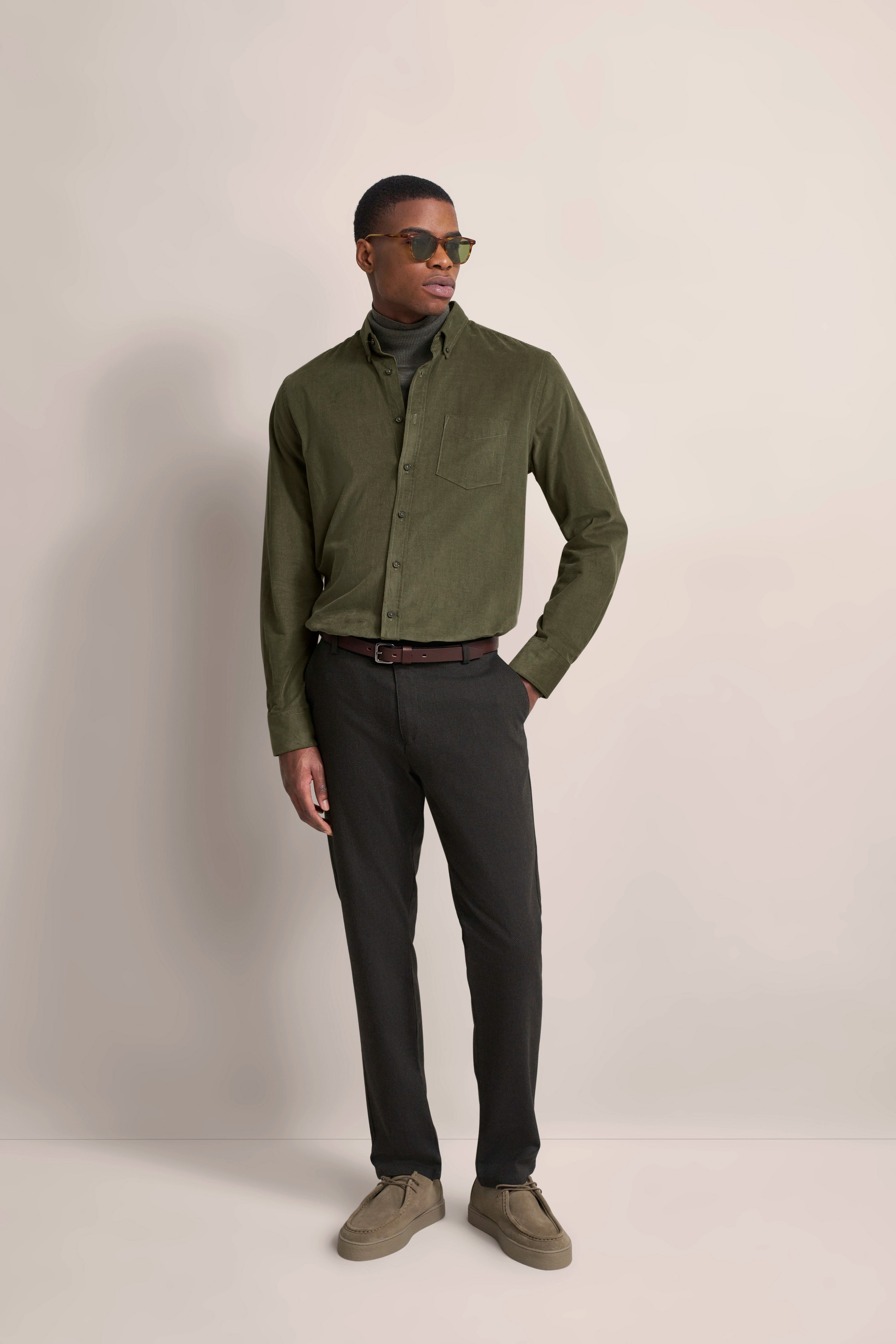 bugatti Model in olivegrünem Hemd und dunkler Hose, lässig posierend mit Sonnenbrille.