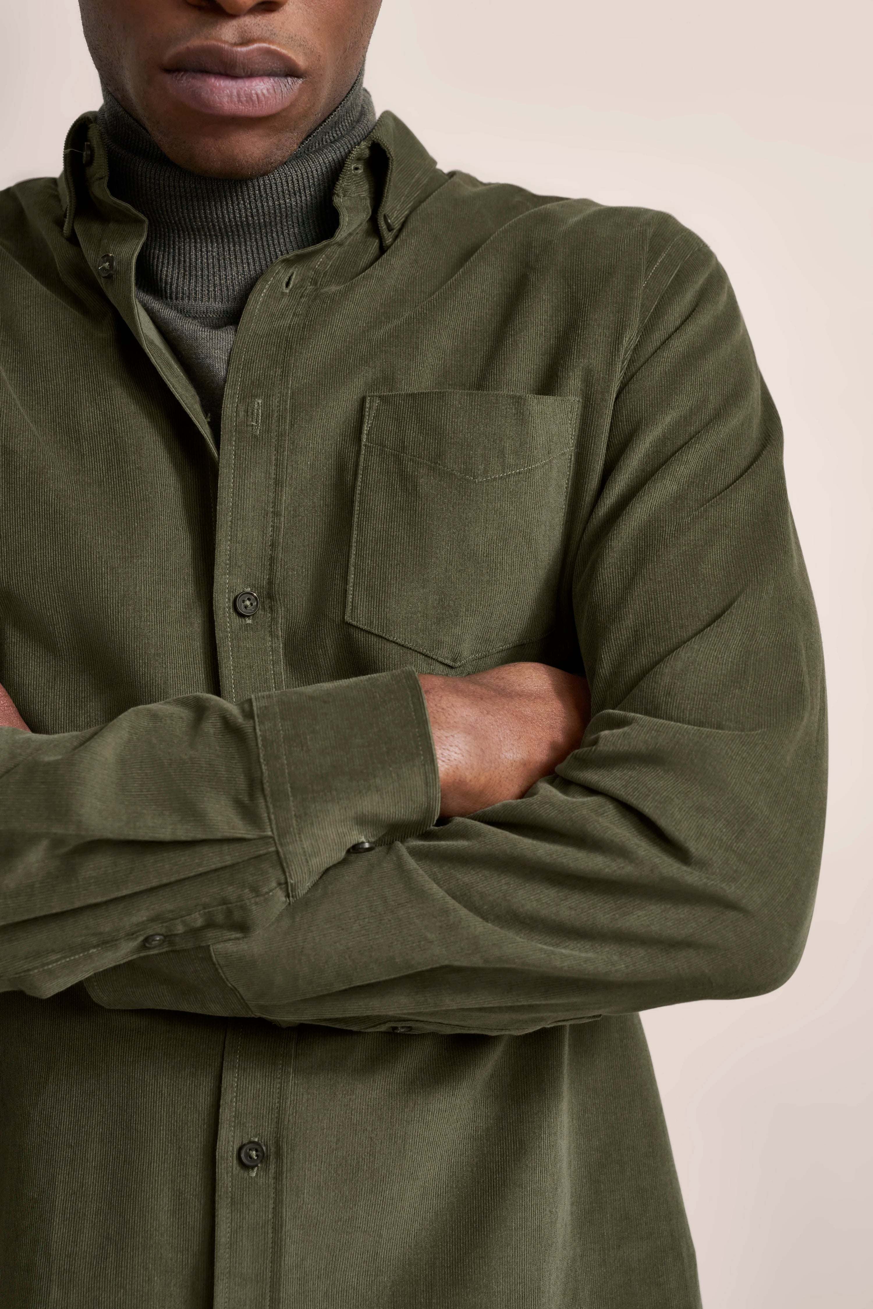 Olivgrünes Hemd über grauem Rollkragenpullover, legeres Modelbild mit verschränkten Armen.
