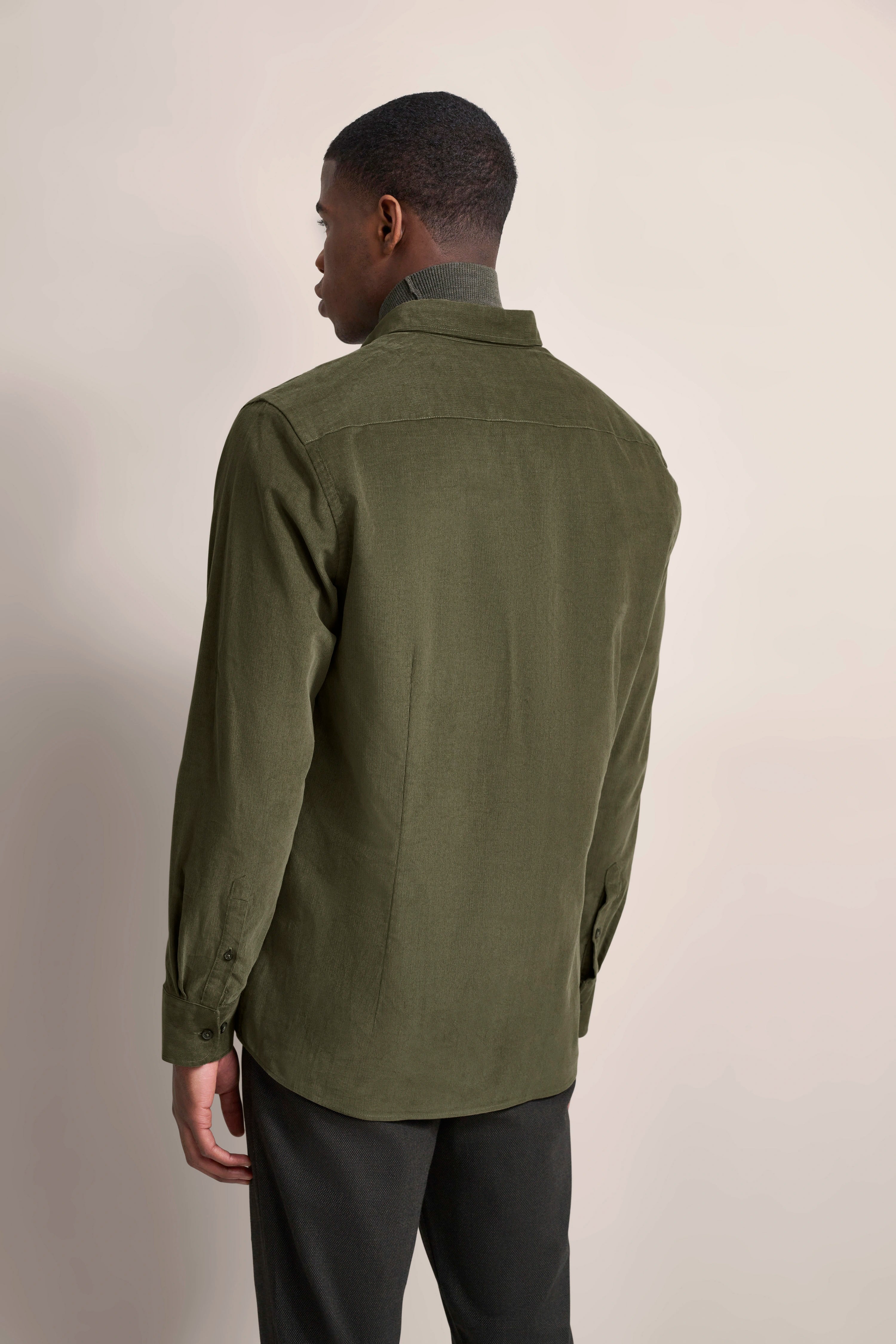 bugatti Modelbild, Mann in olivgrünem Hemd, Rückansicht, entspannte Pose, dunkle Hose.