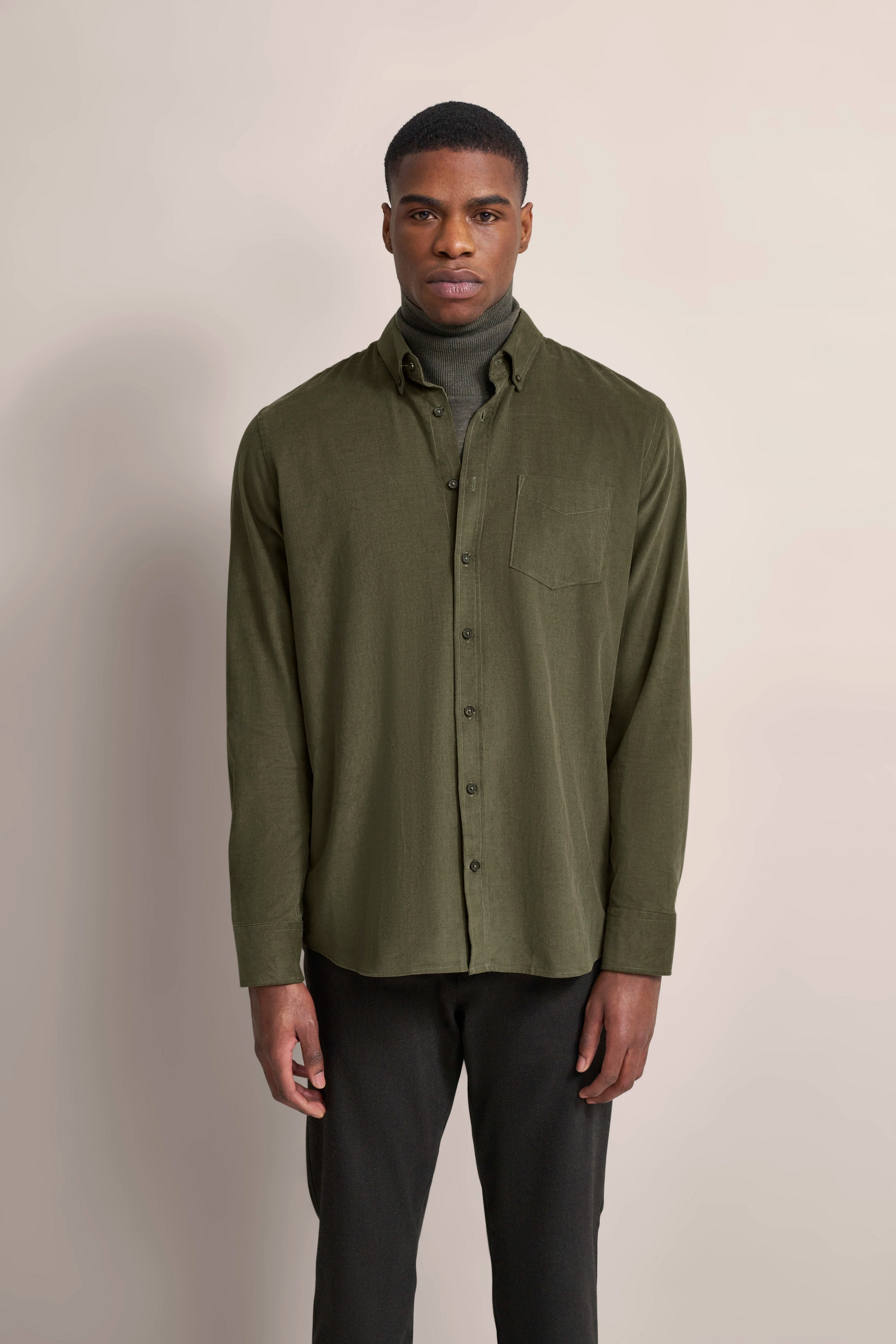 Modelbild: Olivgrünes Hemd über grauem Rollkragenpullover, schwarze Hose. Entspanntes Stehen.