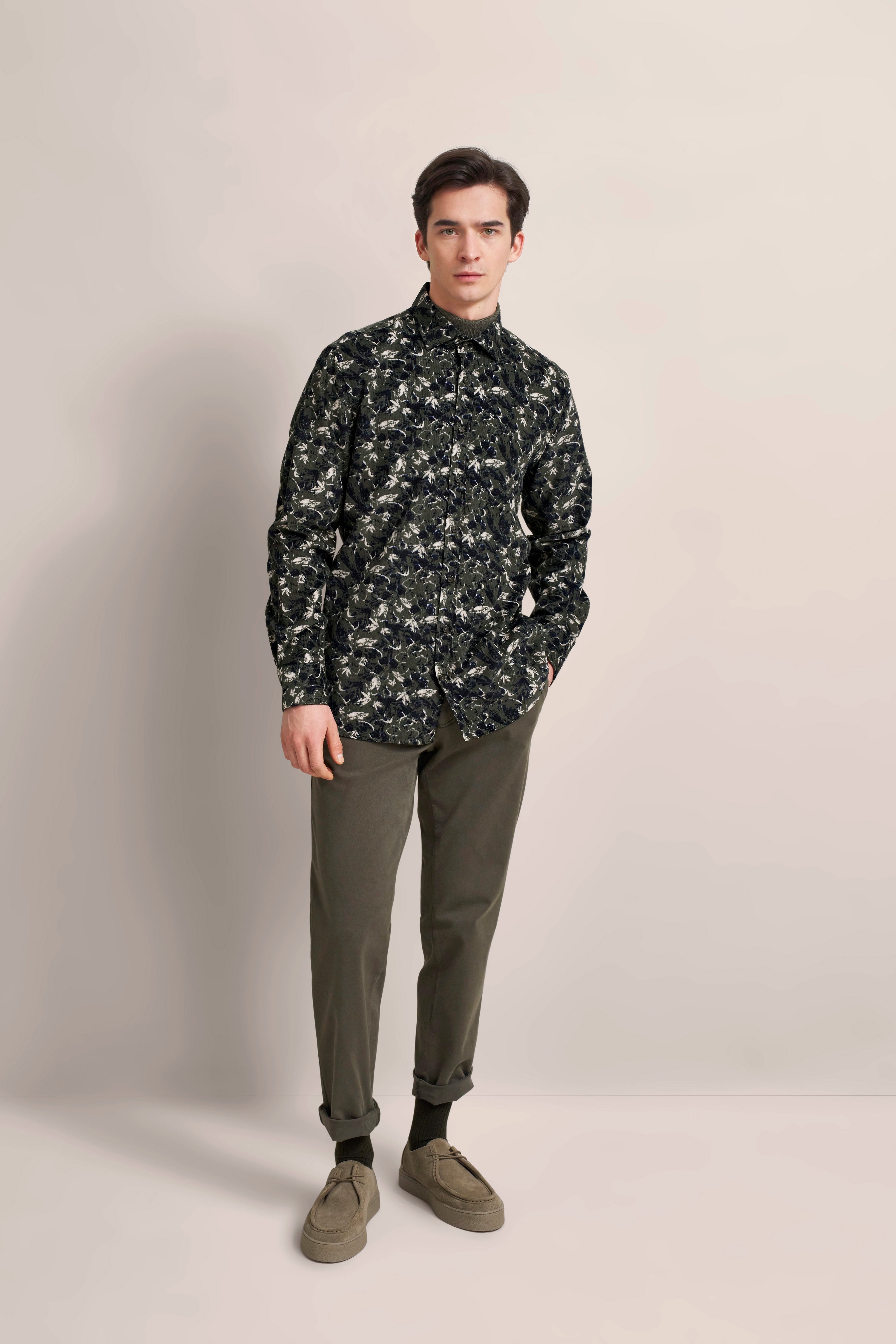 Model wearing patterned black-and-white shirt, olive pants. Casual, hands in pockets. bugatti.