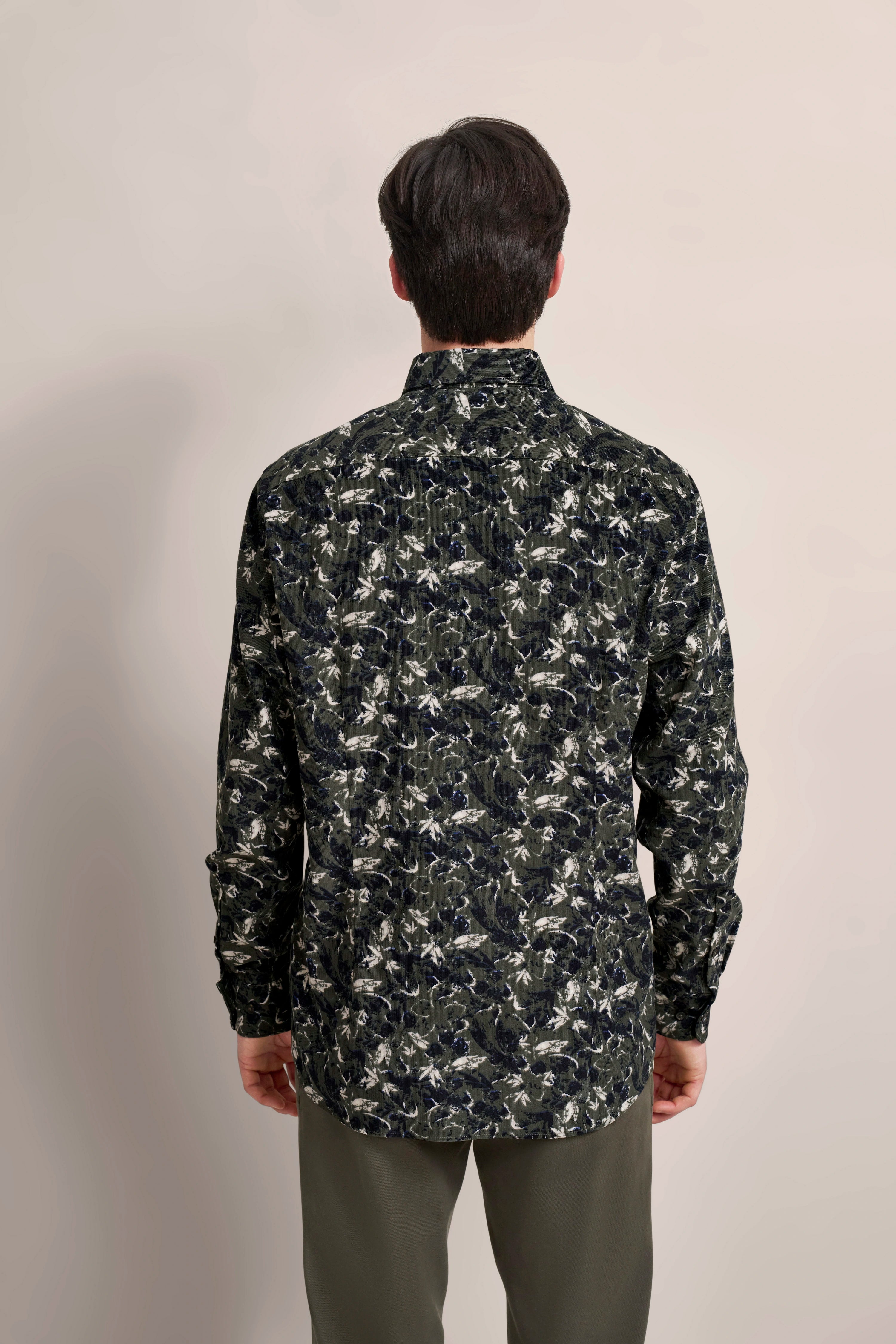 Back view: Model in a long-sleeve dark green floral shirt, paired with olive green trousers.