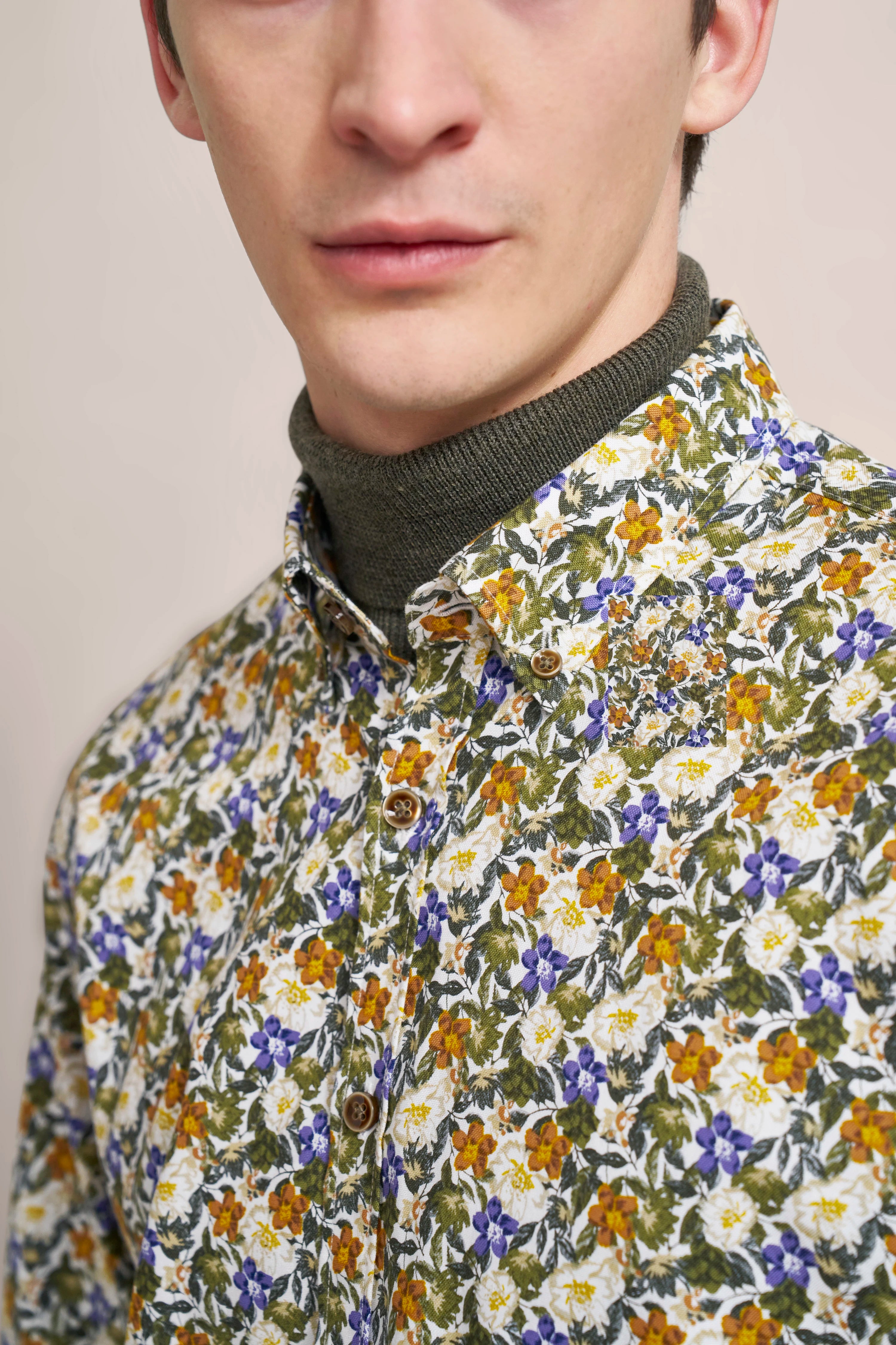 Blumenhemd in Grün, Orange und Blau auf Büstenbild, darunter grüner Rollkragenpullover.