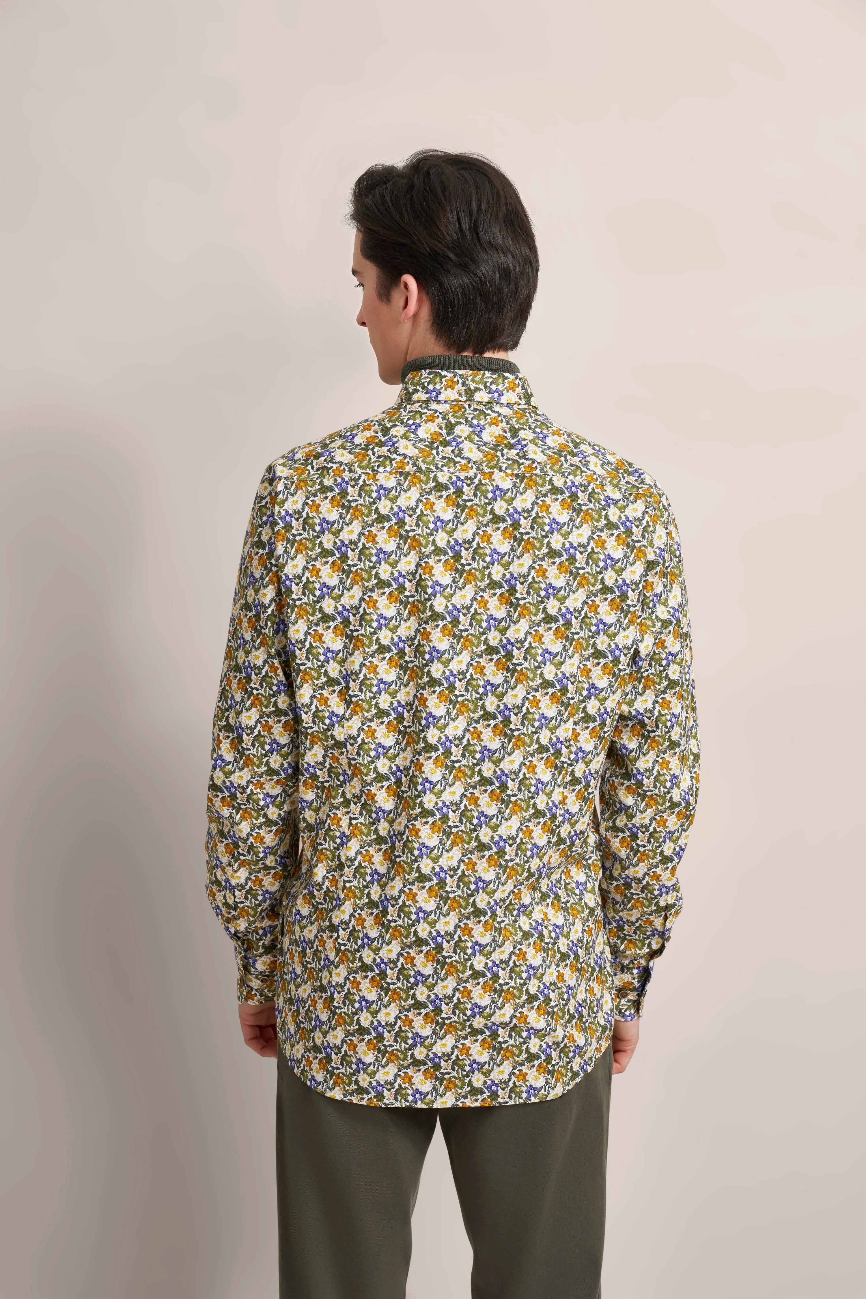 Rückansicht eines Models in floralem Hemd in Gelb, Blau, Grün von bugatti, kombiniert mit grüner Hose.