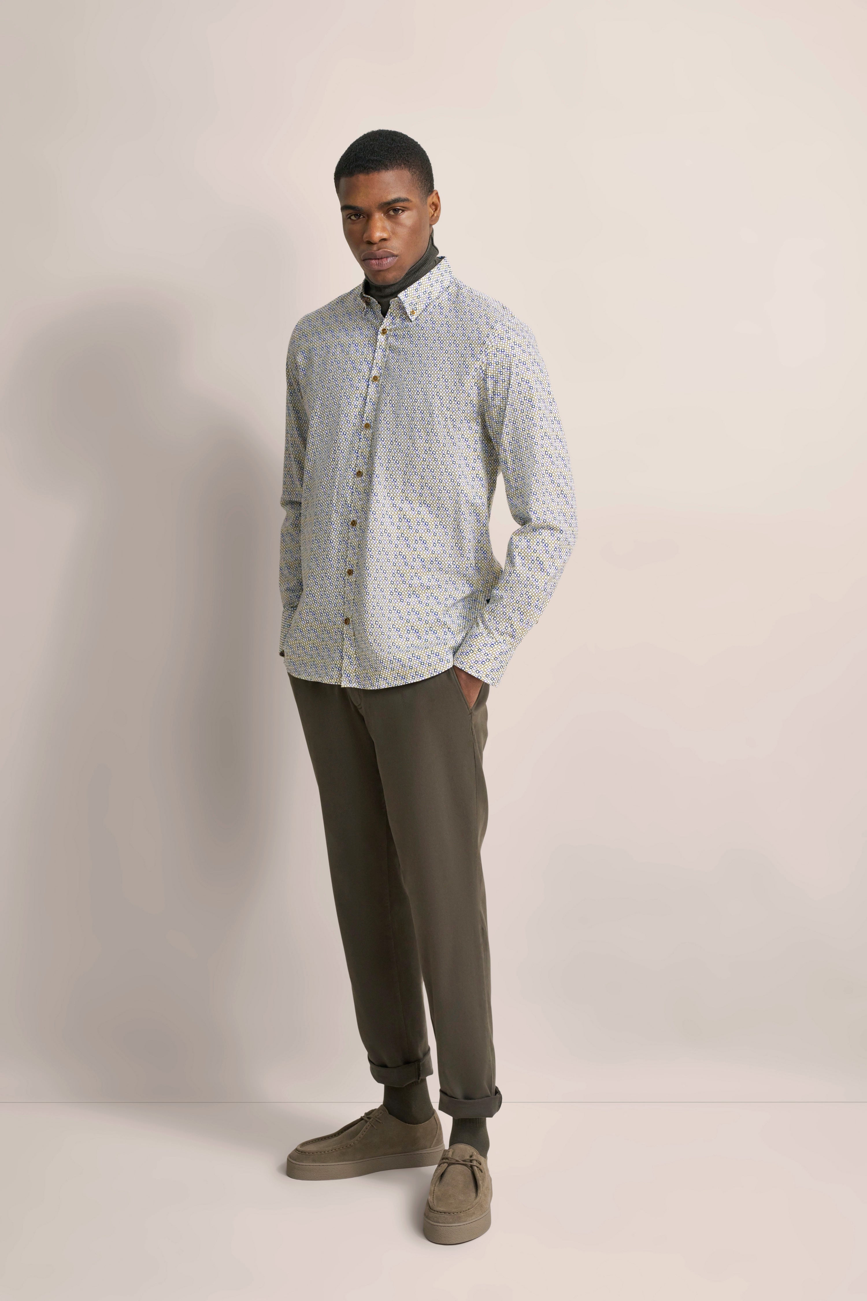 Model trägt bugatti-Hemd mit Muster und olivgrüner Hose, lässige Pose, Hände in den Taschen.