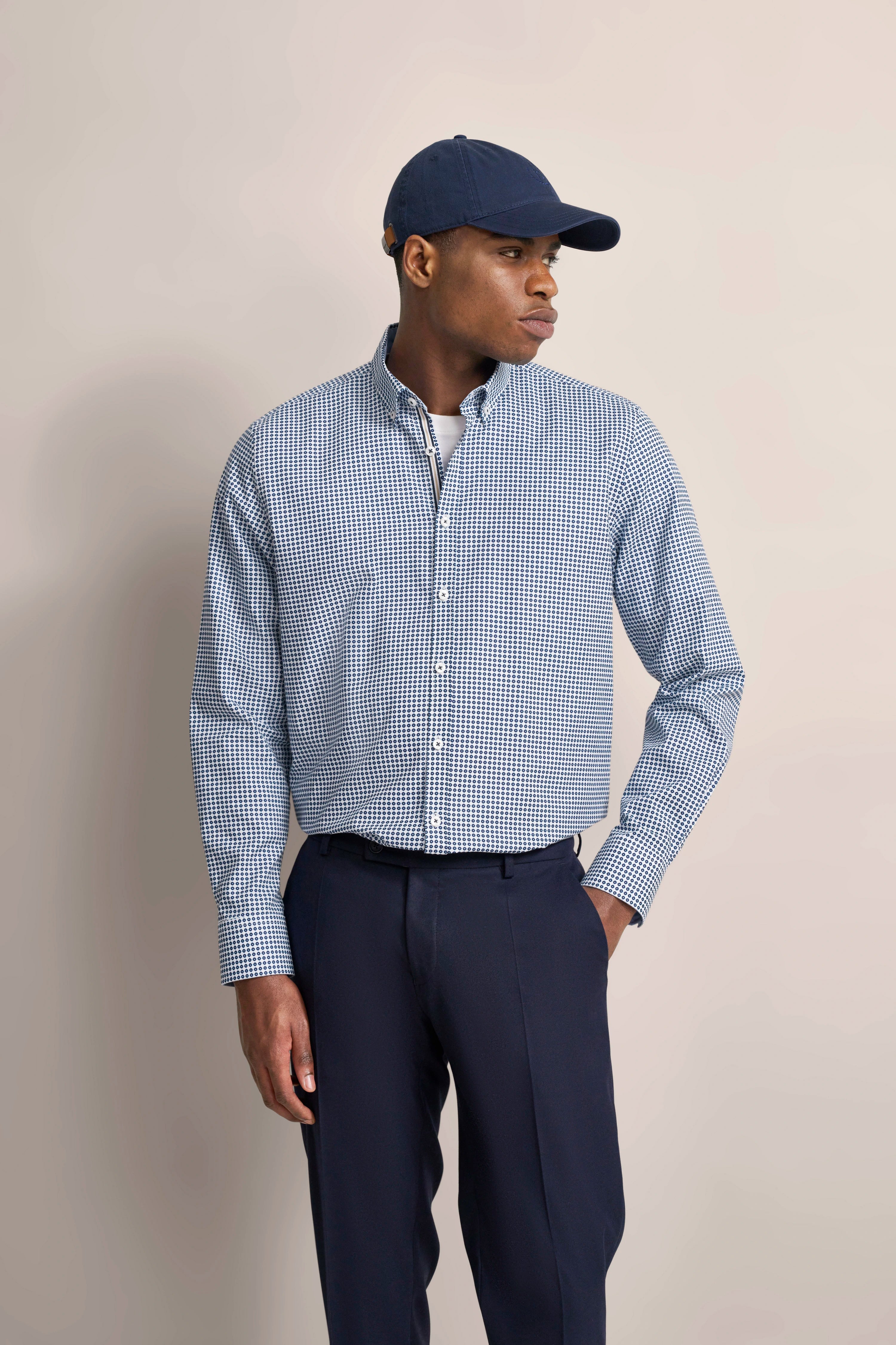 Man in blue-white checkered shirt and navy pants, wearing a blue cap, modeling sideways.