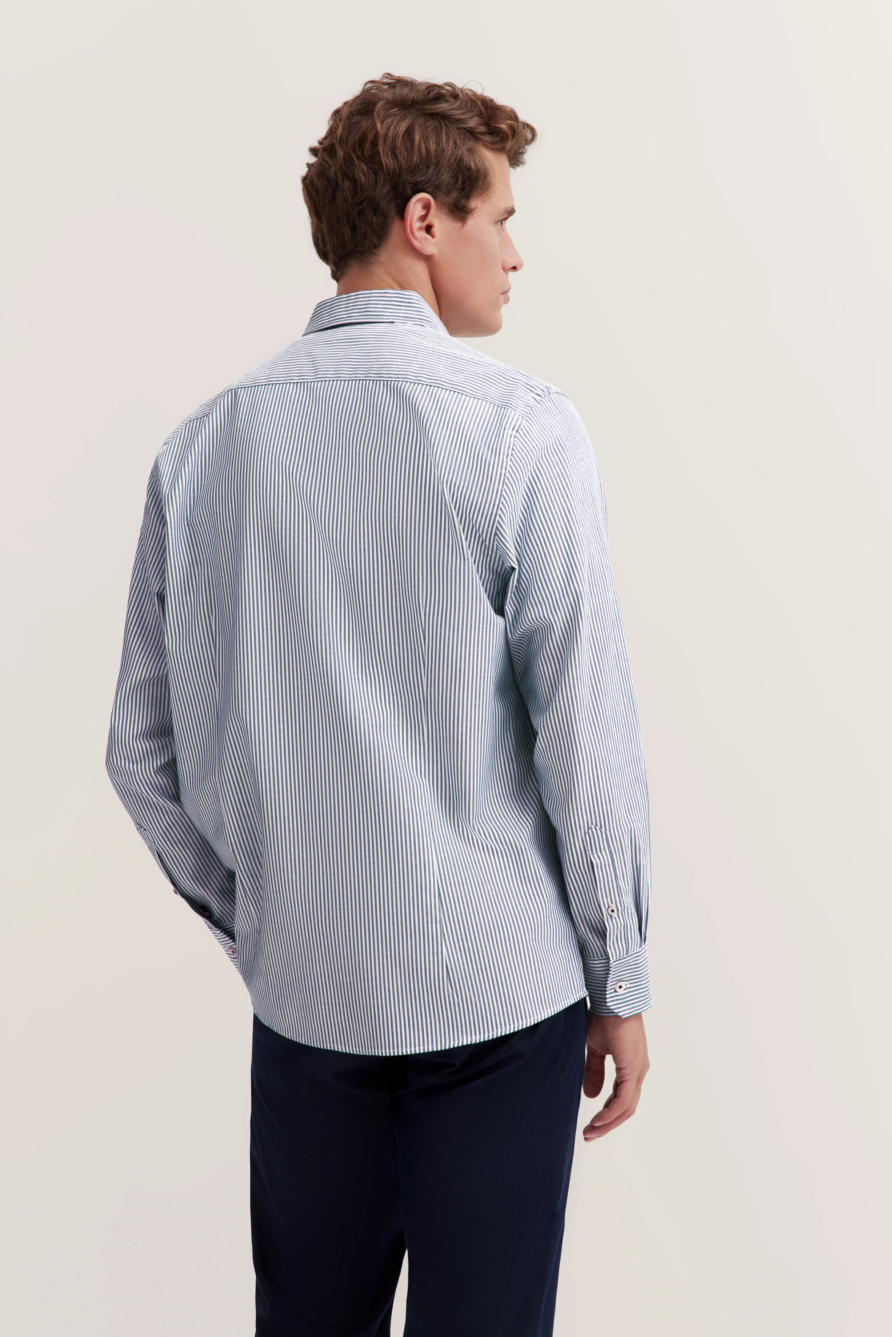 Bugatti Hemd, blau-weiß gestreift, langärmelig. Model von hinten, legeres Posing.
