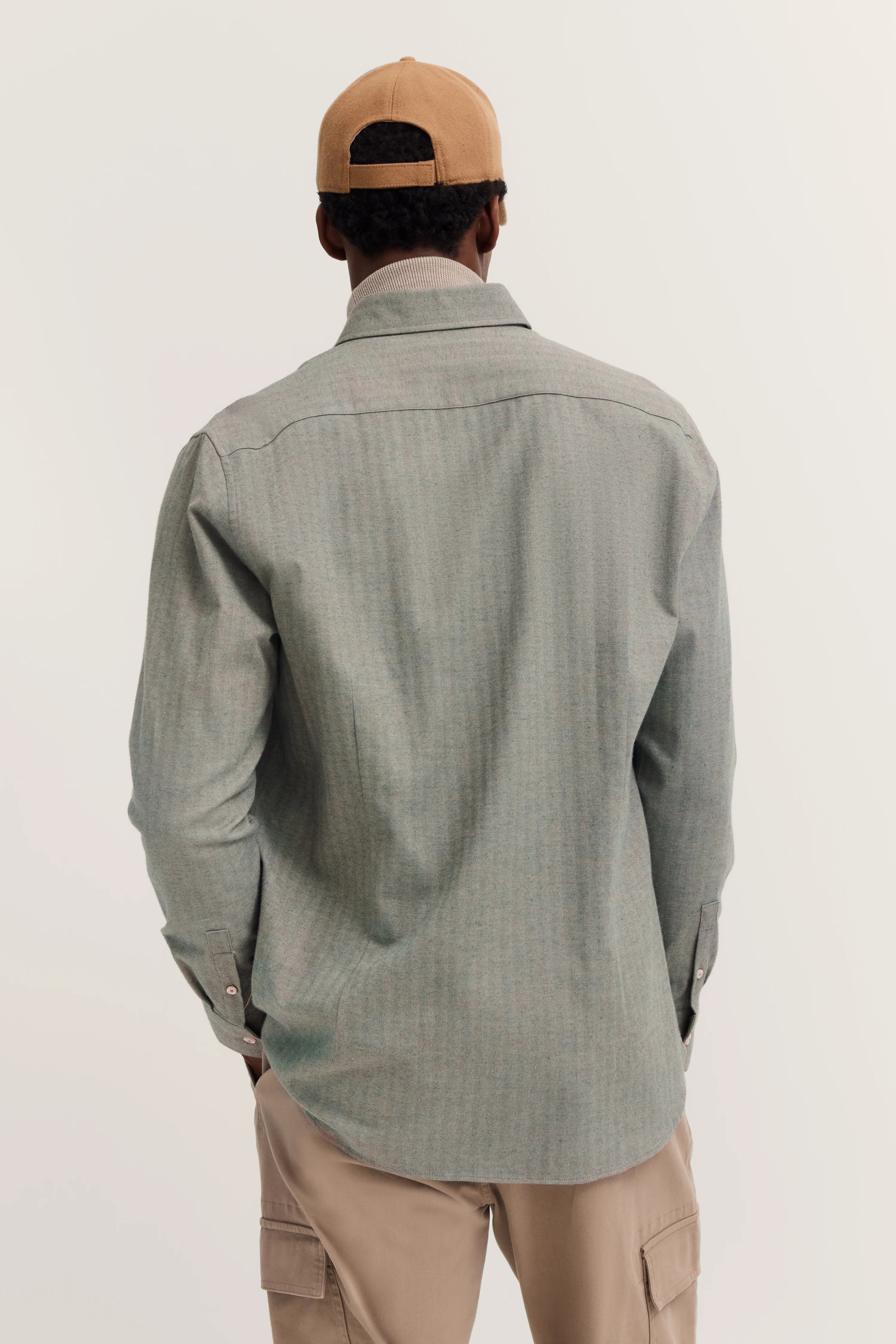 Model wears grey bugatti shirt and beige cap, back view, casual outfit.