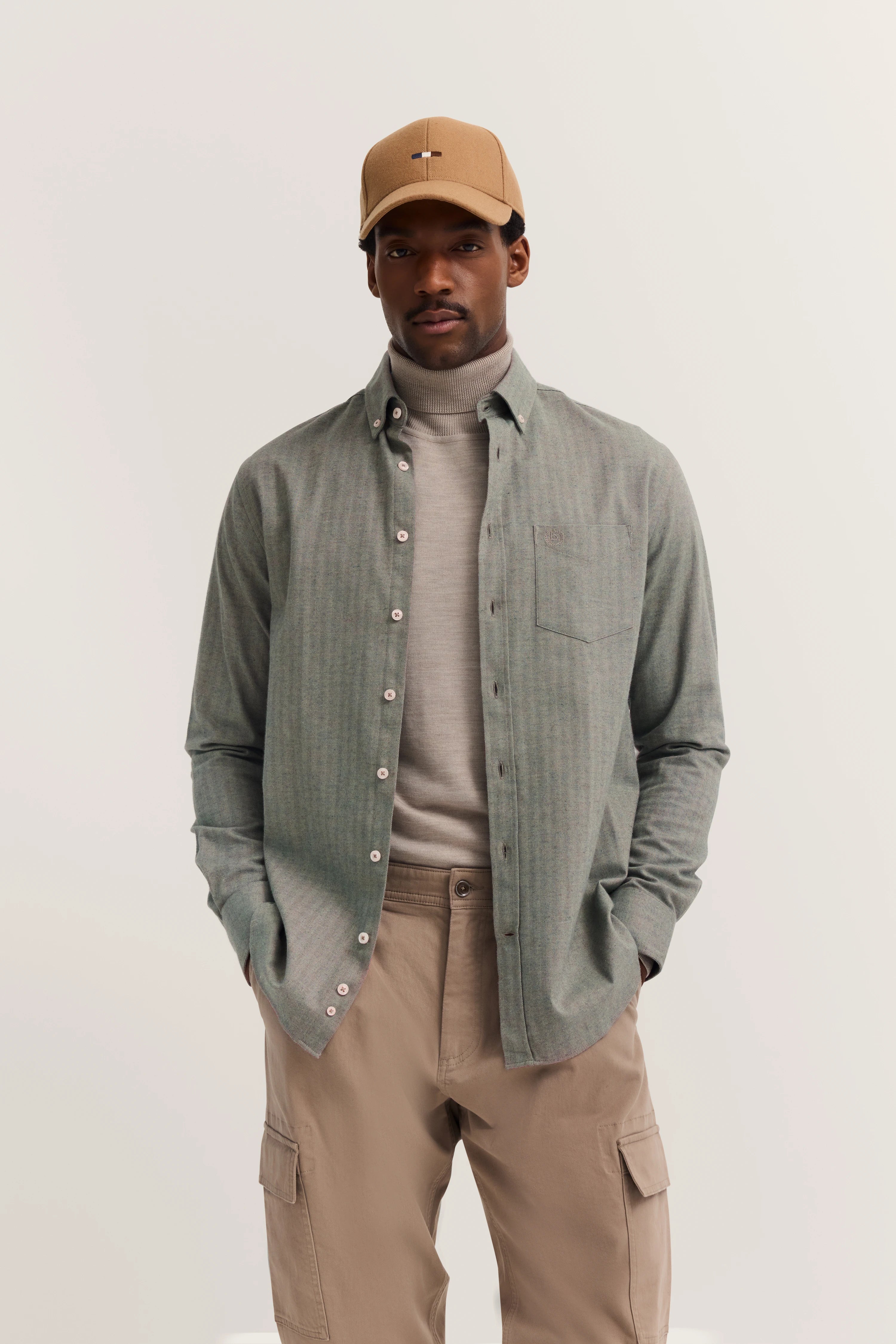 Model in beige pants, gray turtleneck, olive shirt, hands in pockets, embodying bugatti's effortless style.