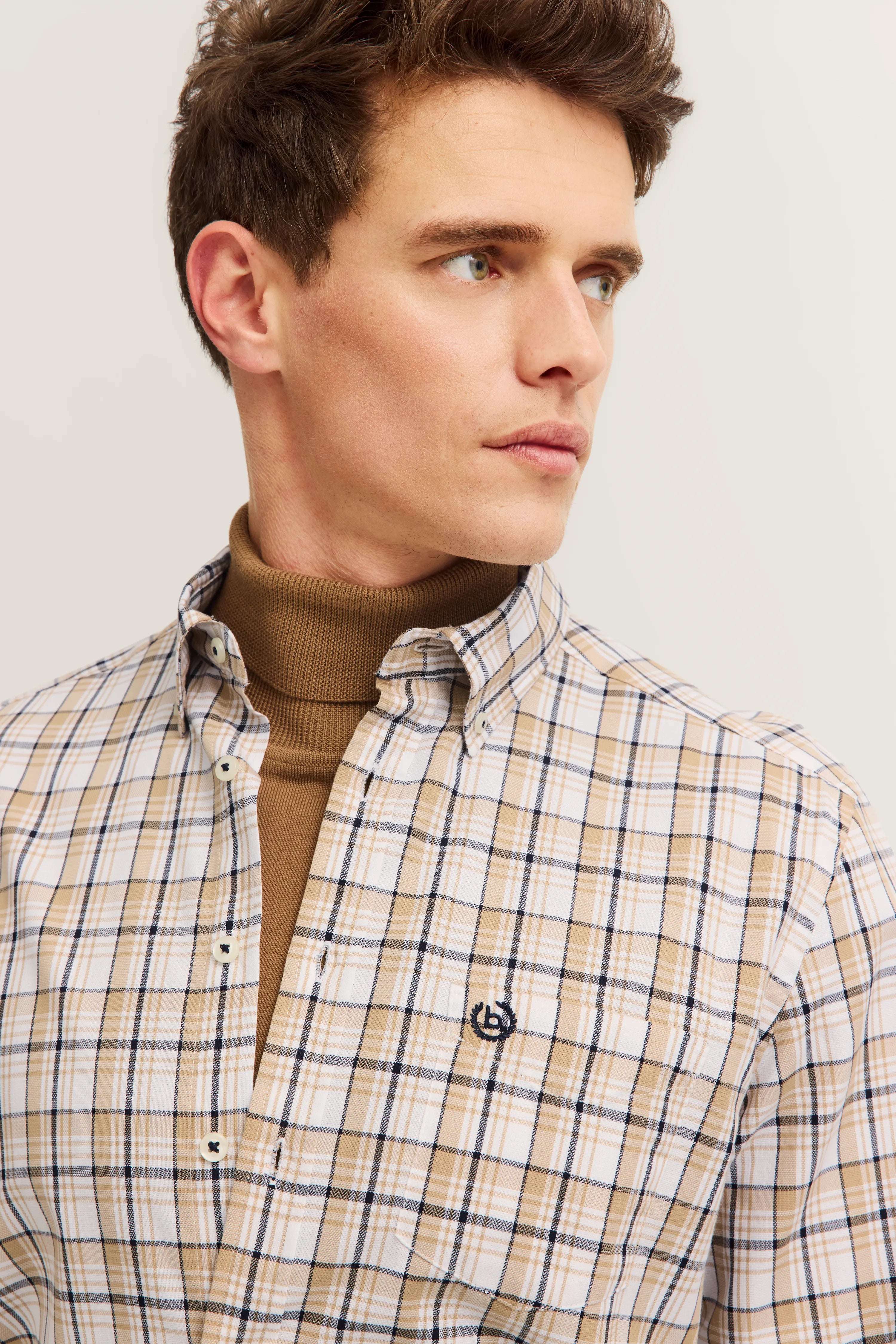 Kariertes bugatti Hemd in Beige-Braun, über einem braunen Rollkragenpullover, Modelbild mit Seitenblick.
