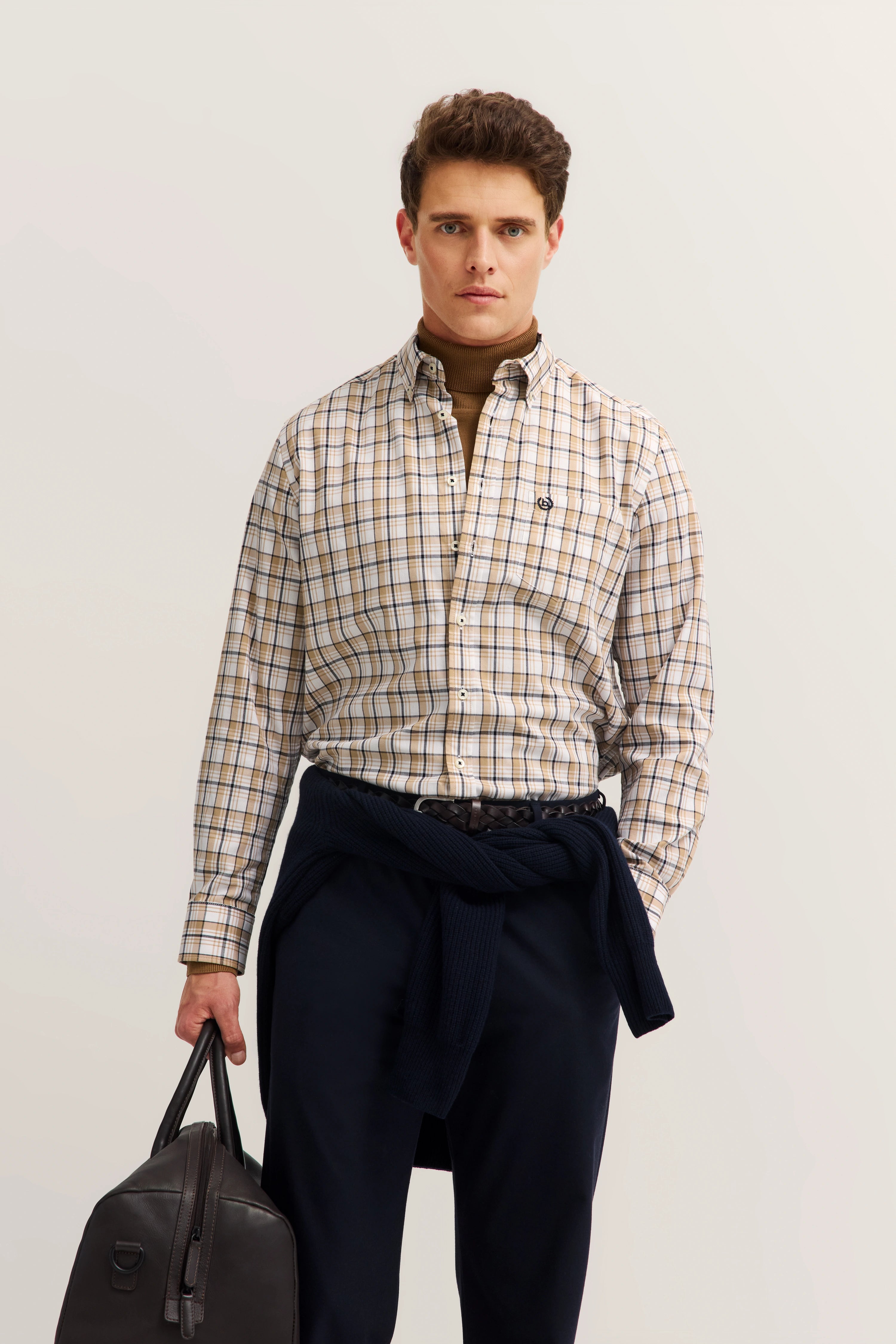 "Model in kariertem bugatti-Hemd mit Rollkragen, marineblauer Hose und Tasche, posierend mit entspanntem Blick."