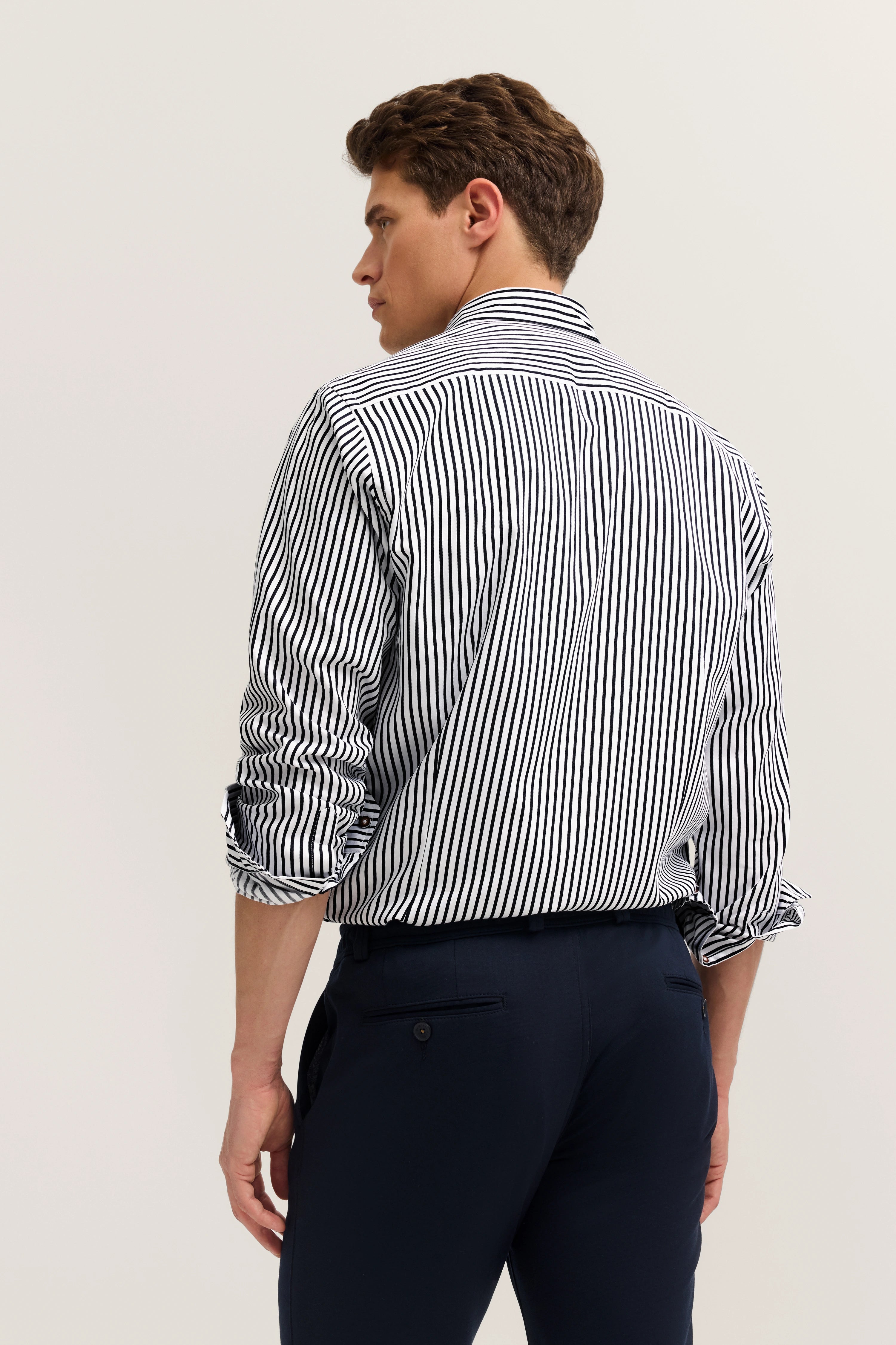bugatti model: man in striped shirt & navy pants, relaxed pose from behind, exuding Italian elegance & style.