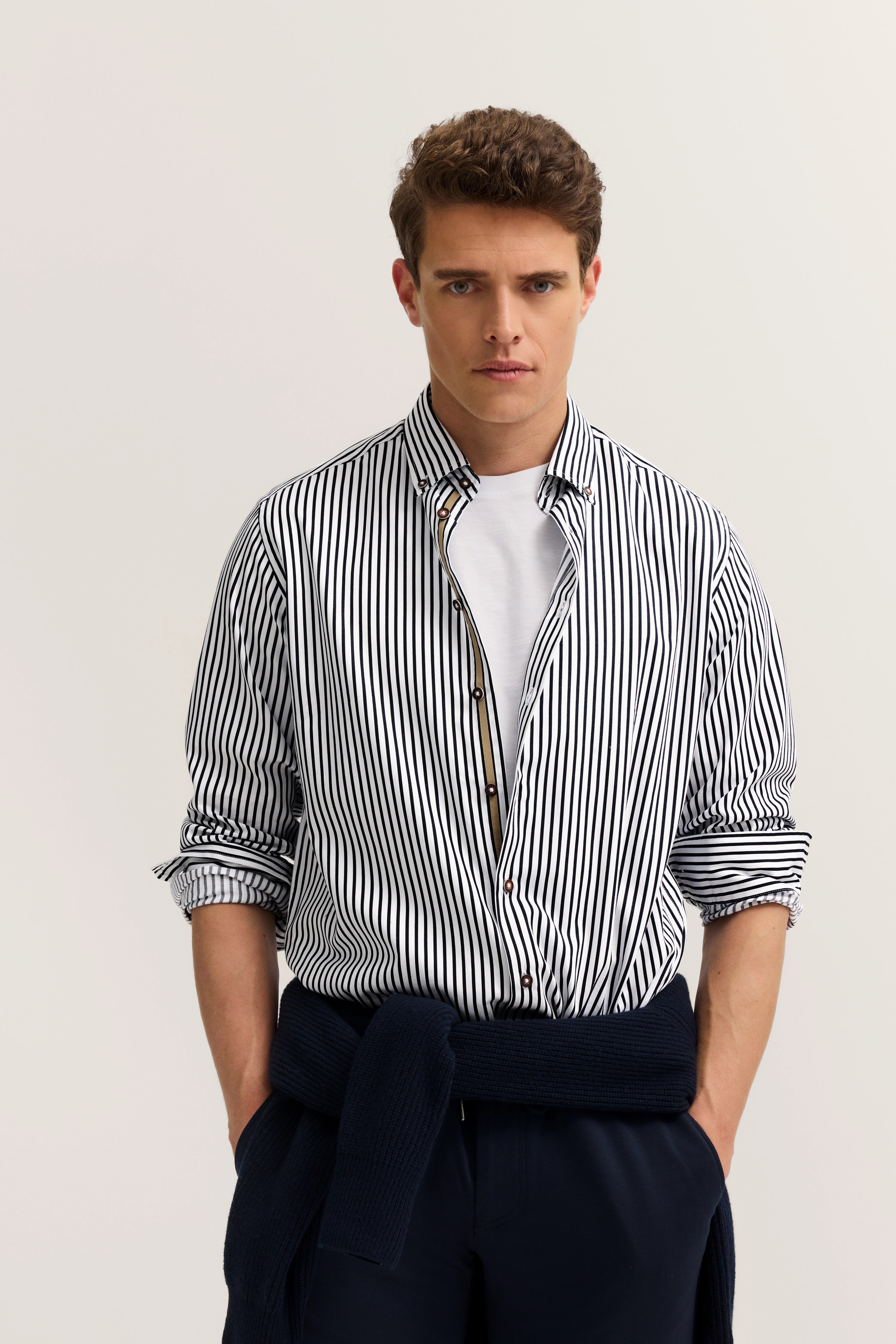 Model in striped shirt, white tee, blue pants, casual pose, bugatti style.