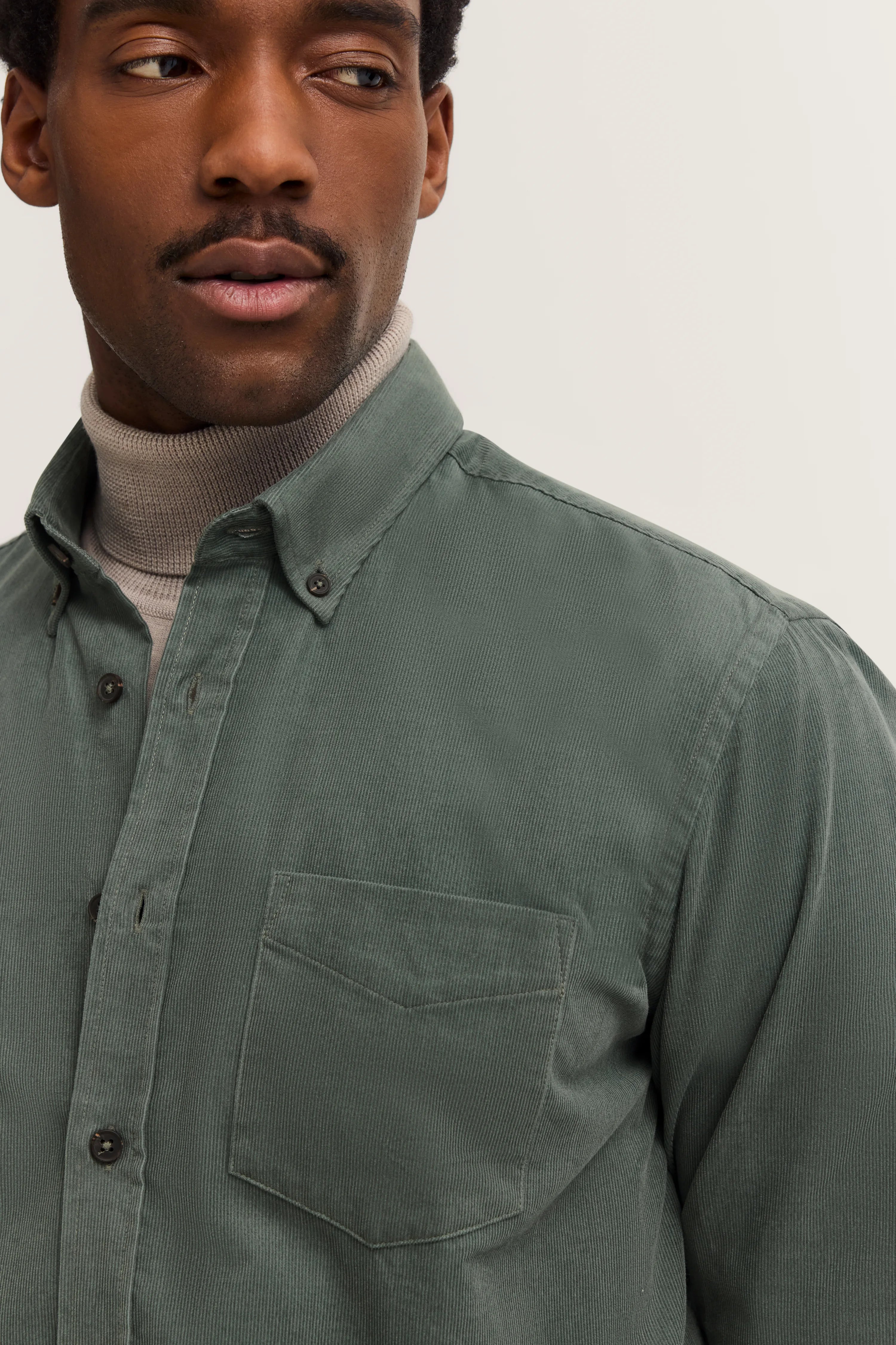Green bugatti shirt over gray turtleneck, model image, relaxed pose.