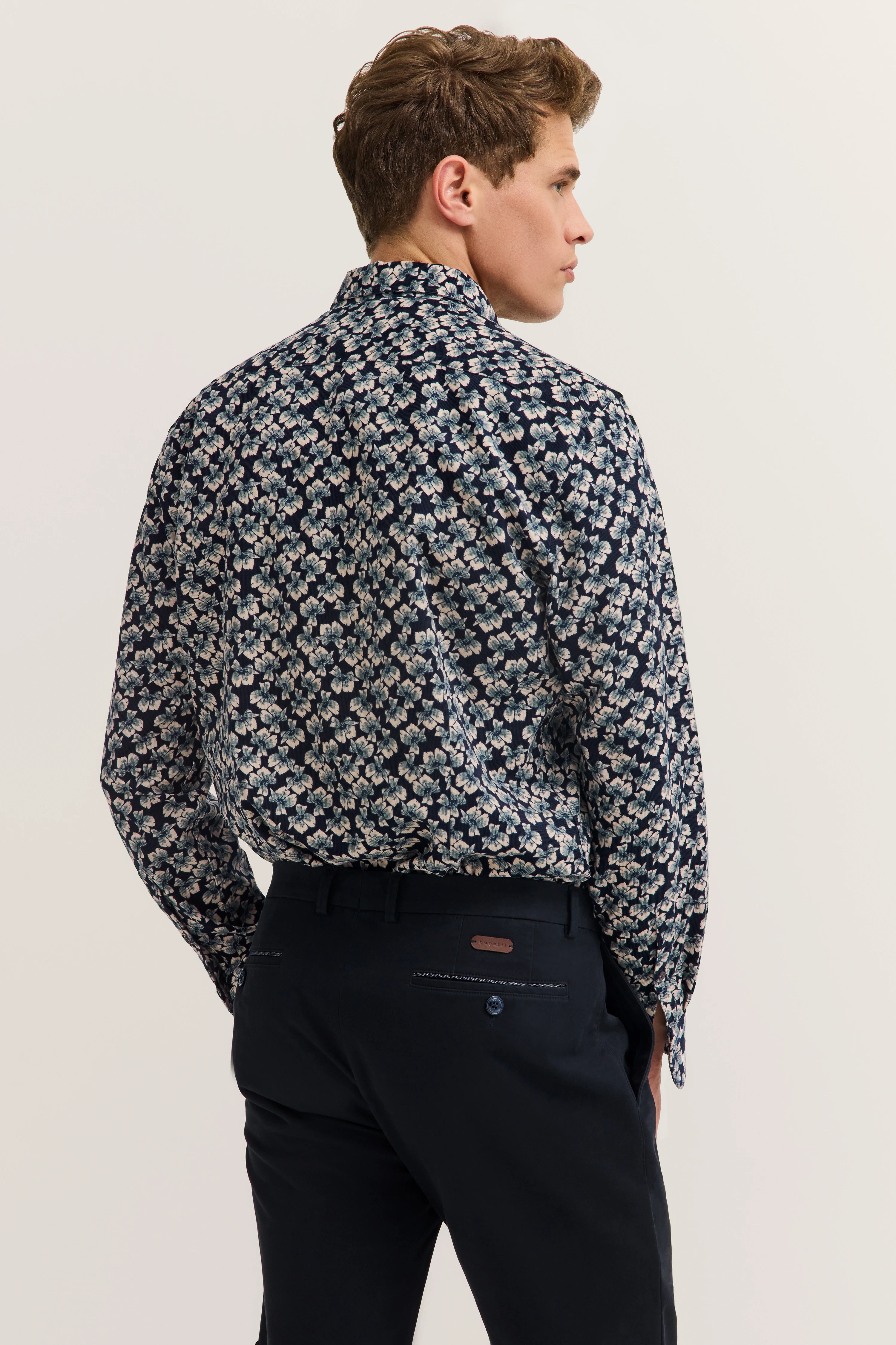 Dark blue floral shirt with black pants, model in rear view pose, bugatti style.