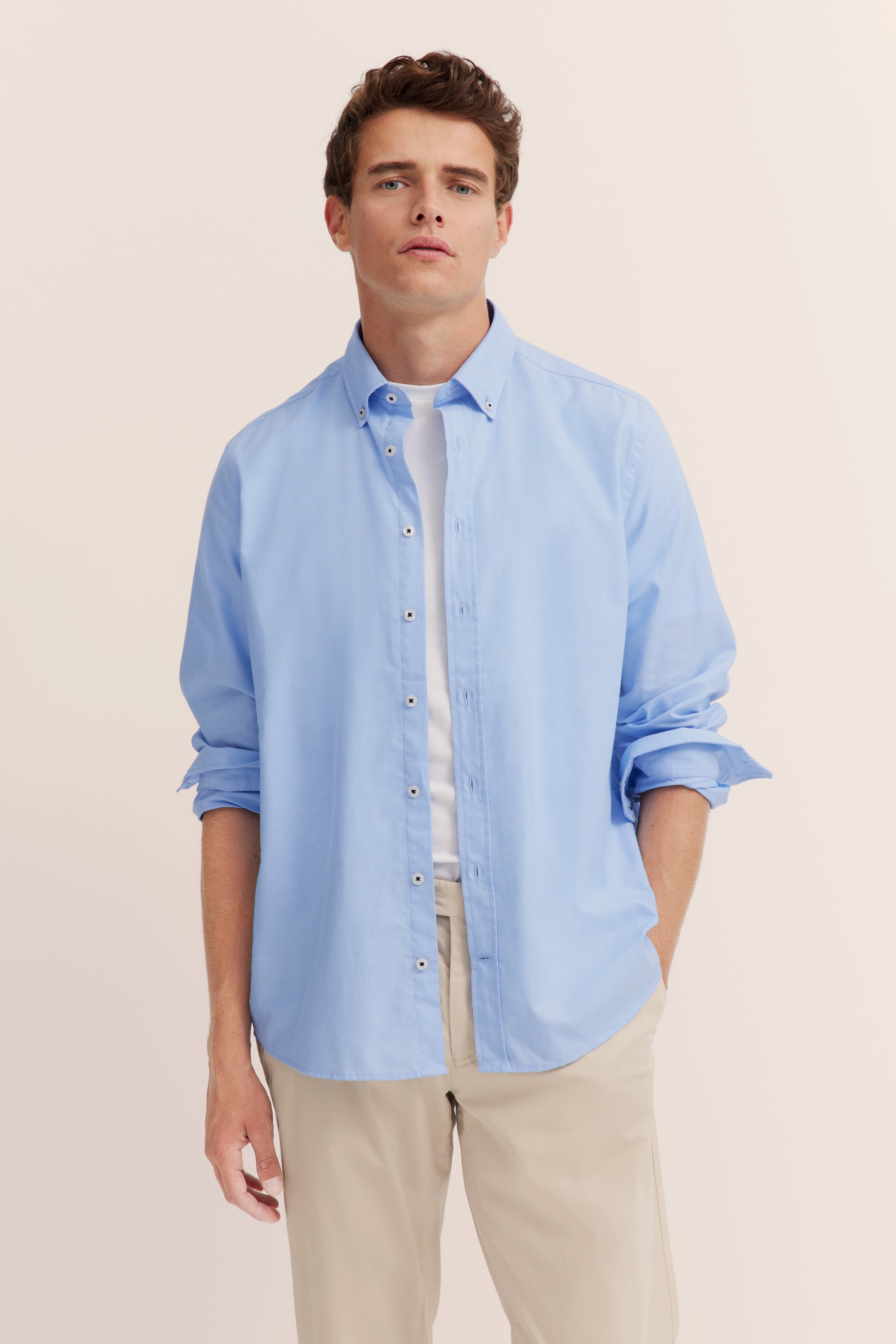 Blaues Hemd über weißem T-Shirt mit beigen Hosen, Model steht leger.