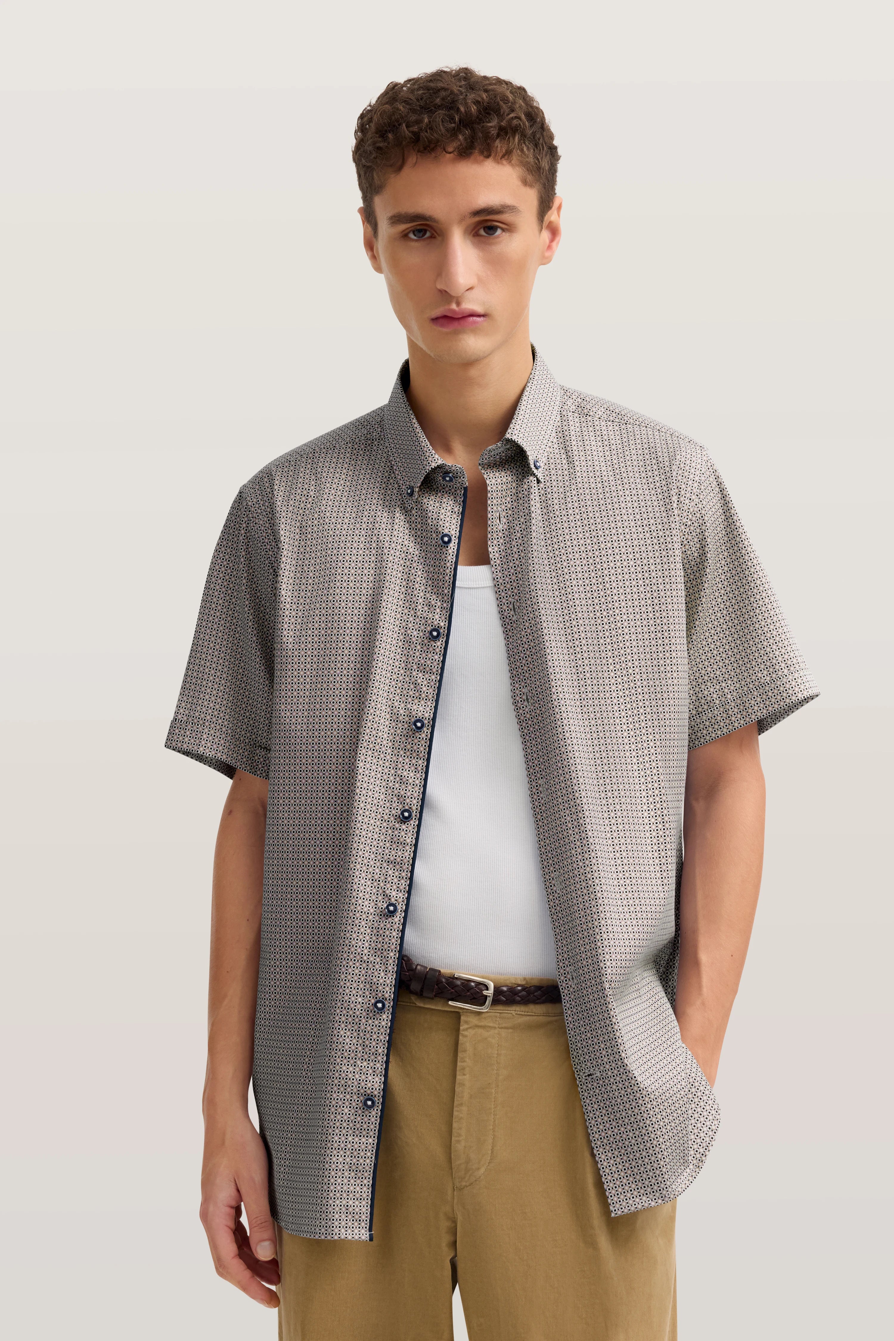 Kurzarmhemd mit Muster, beigefarbene Hose, legeres Modelbild, entspannte Pose.