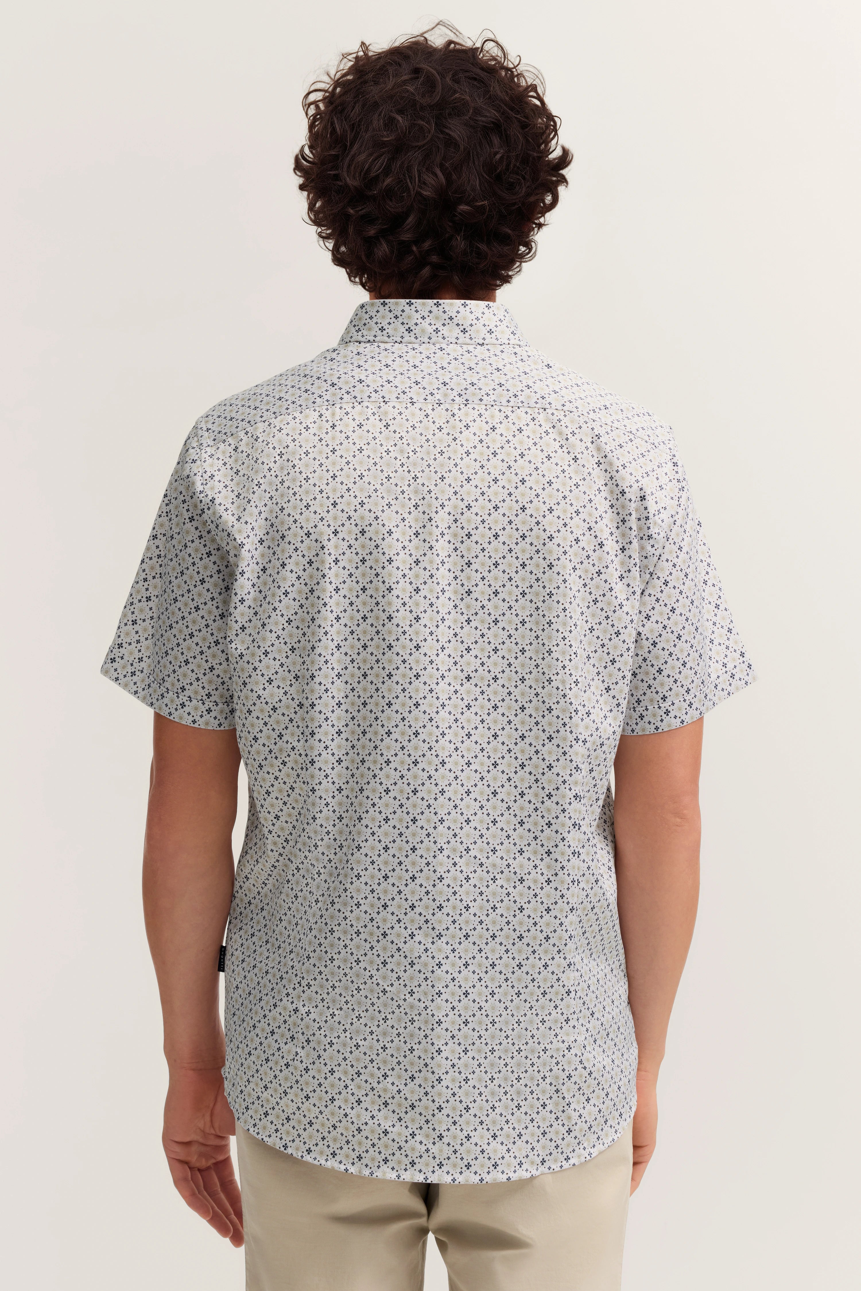 Rückansicht: Kurzarmhemd mit blauem Muster auf weißem Grund, beige Hose, legeres Modelbild.