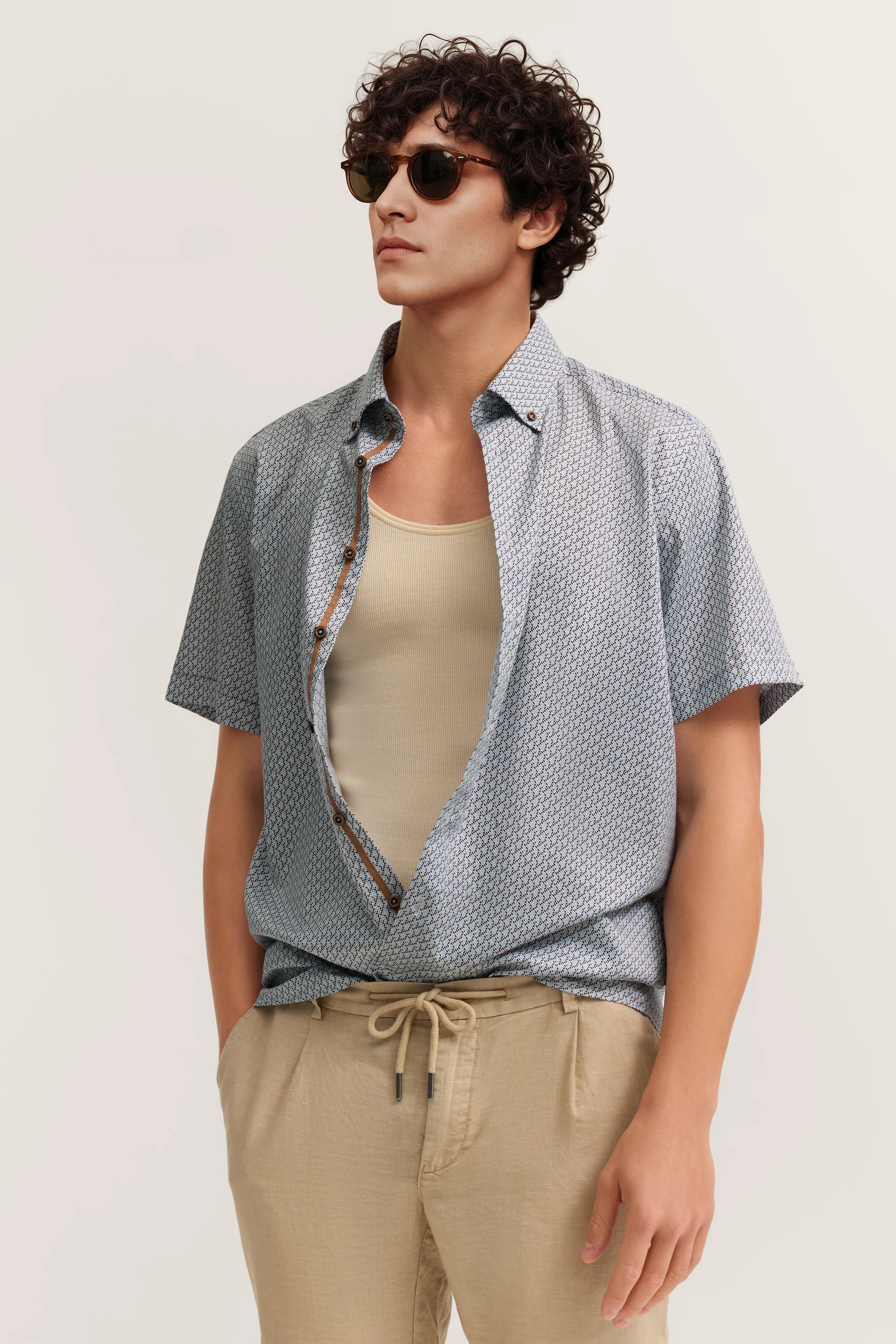 Lässiges Model in offenem gemustertem Hemd, beigem Tanktop und hellen Hosen, bugatti Stil.