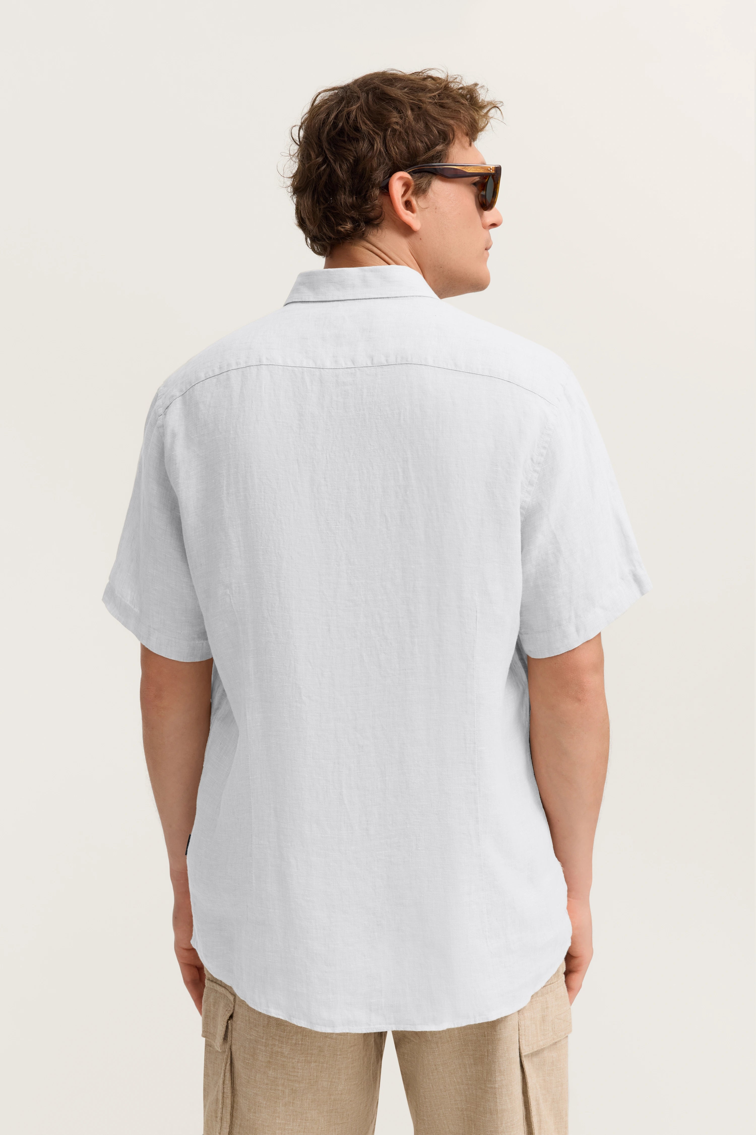 Weiße Kurzarm-Leinenhemd von bugatti, beige Cargoshorts, Rückansicht Model mit Sonnenbrille.