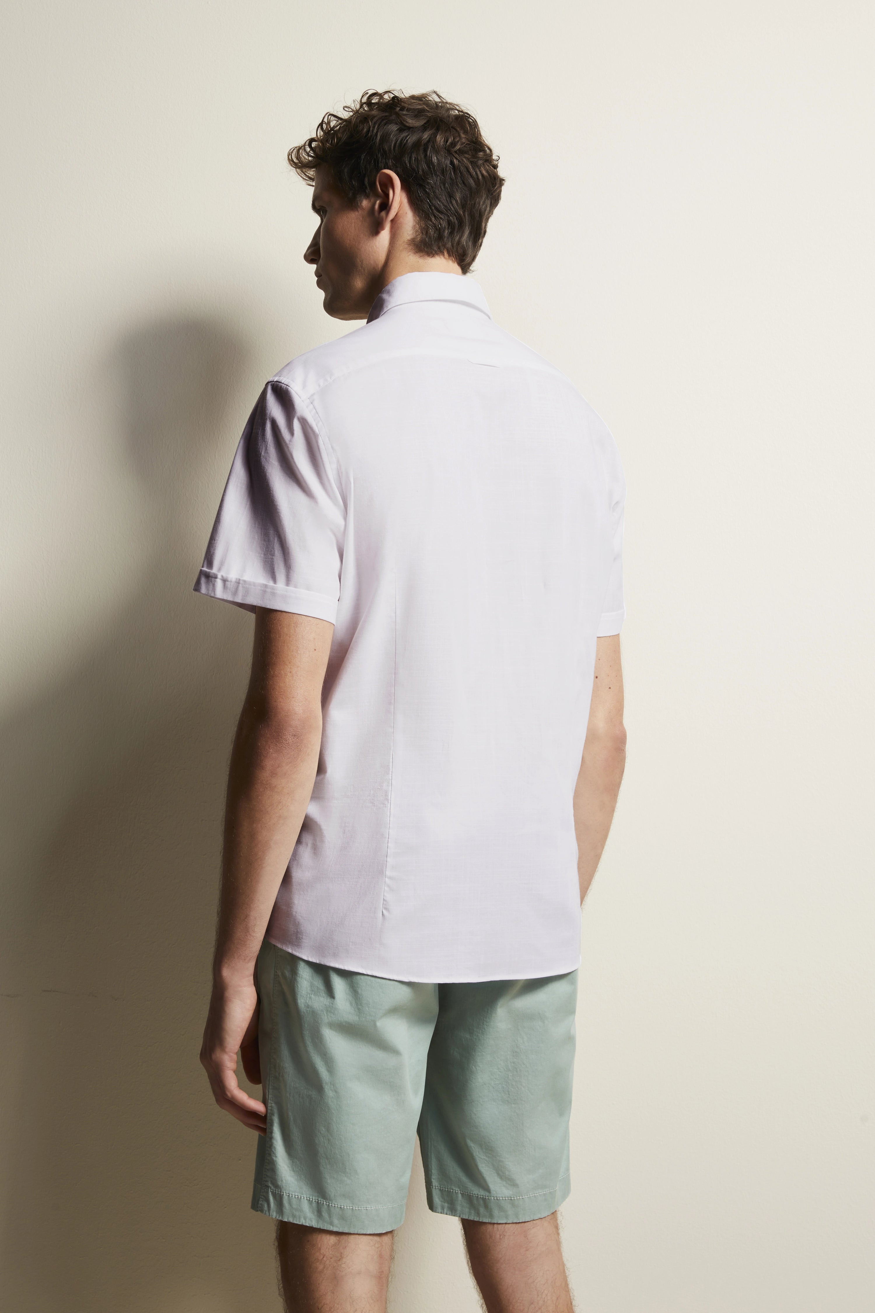 Model rear view in white shirt and mint shorts, casual pose.