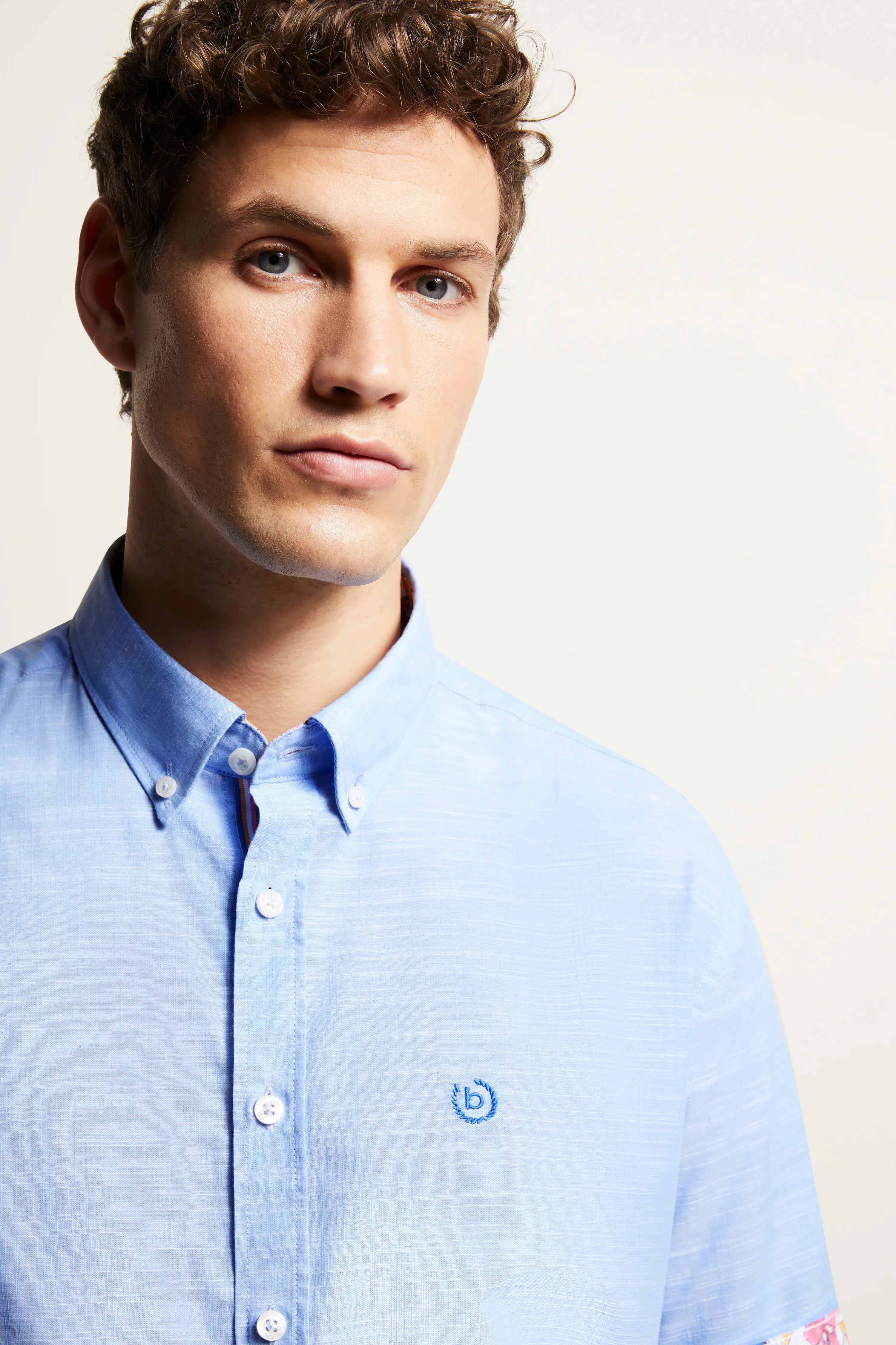 Bust of a man in a light blue bugatti shirt with button placket and logo.