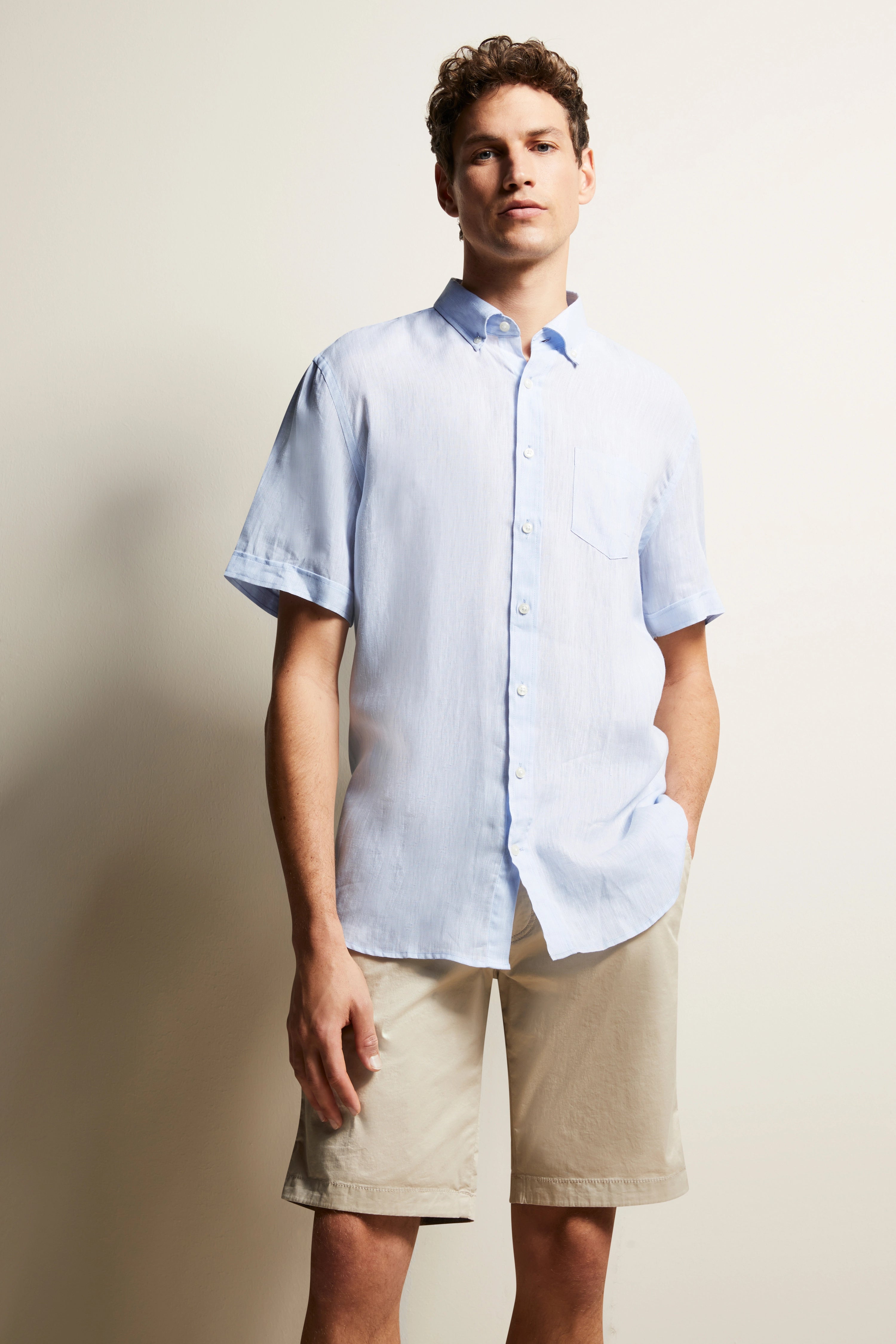 Elegantes Modelbild: Hellblaues Kurzarmhemd und beige Shorts, entspanntes Posing.