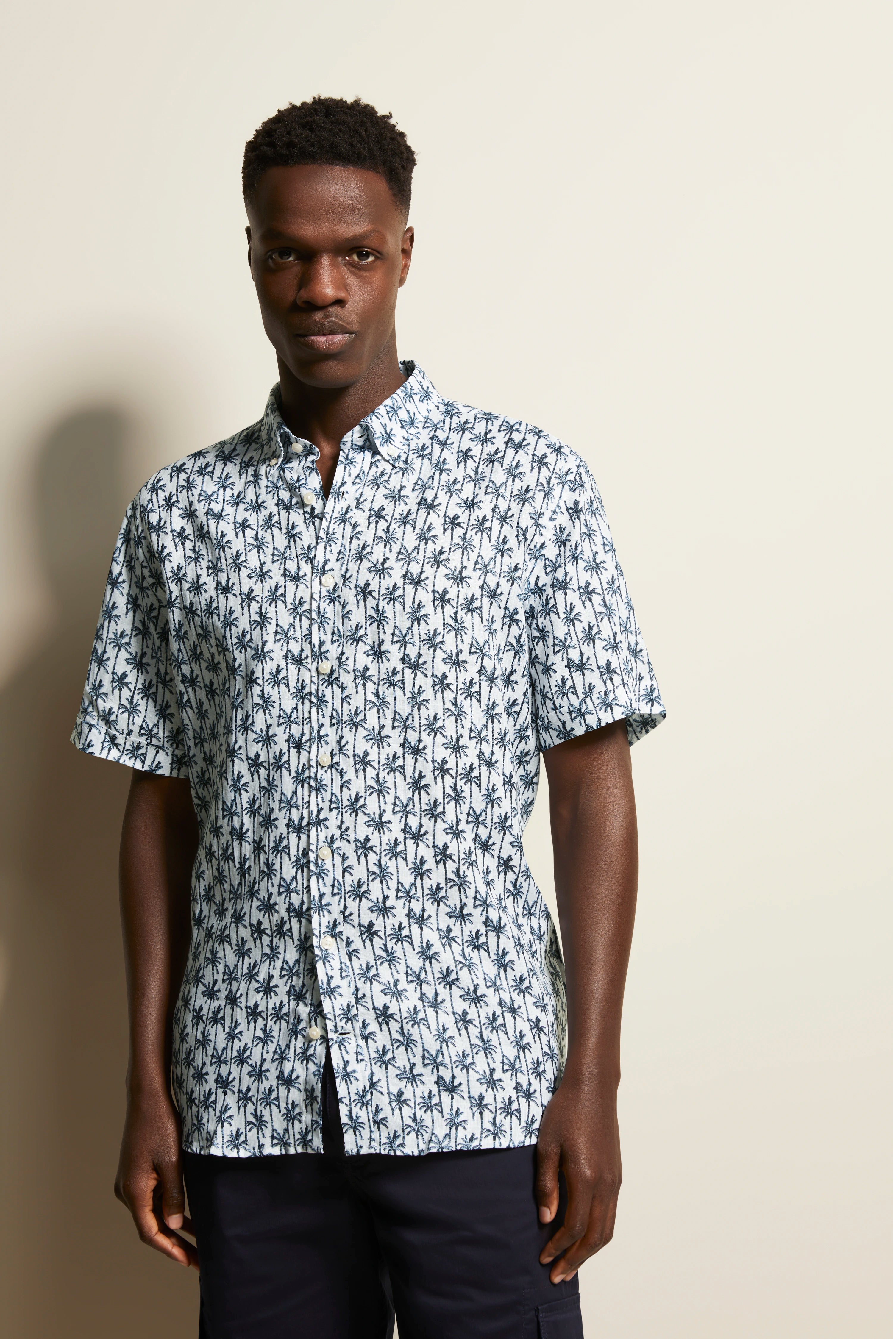 Model wearing bugatti short-sleeve shirt with blue-white palm pattern, standing pose.