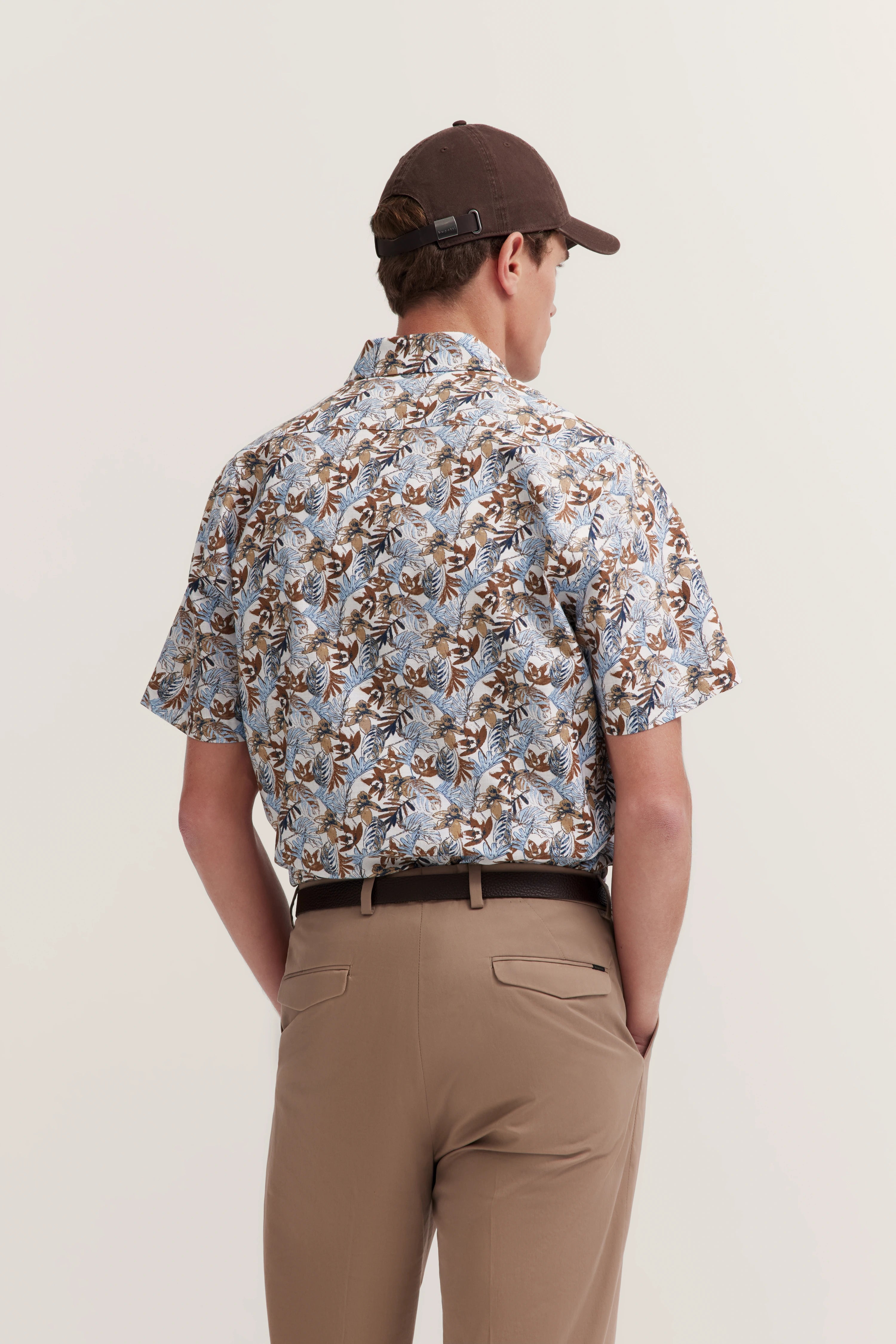 Model draagt florale bugatti overhemd en beige chino, rugaanzicht, ontspannen pose.