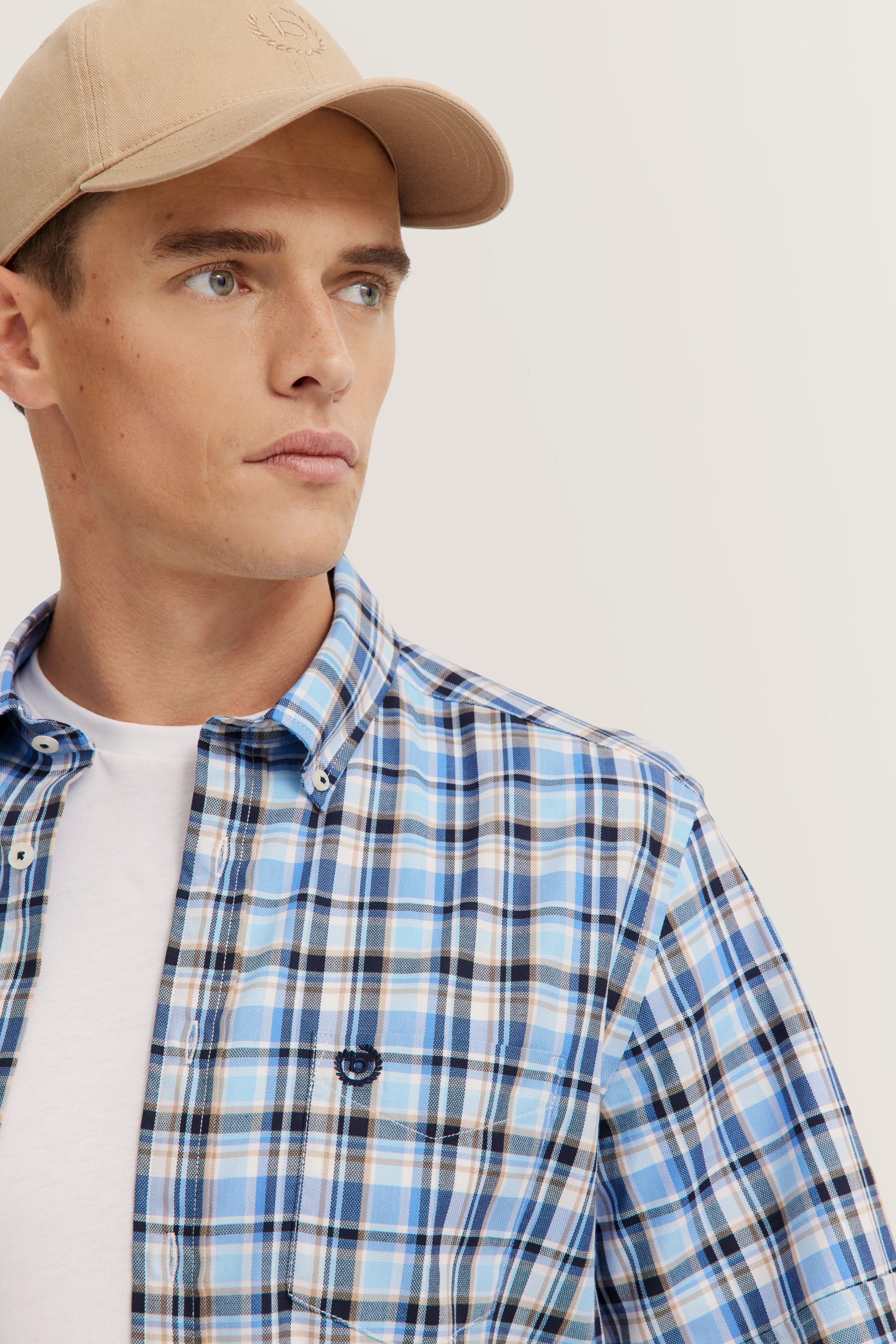 Model trägt blau kariertes bugatti-Hemd und beige Kappe, legeres Bild, entspannter Look.