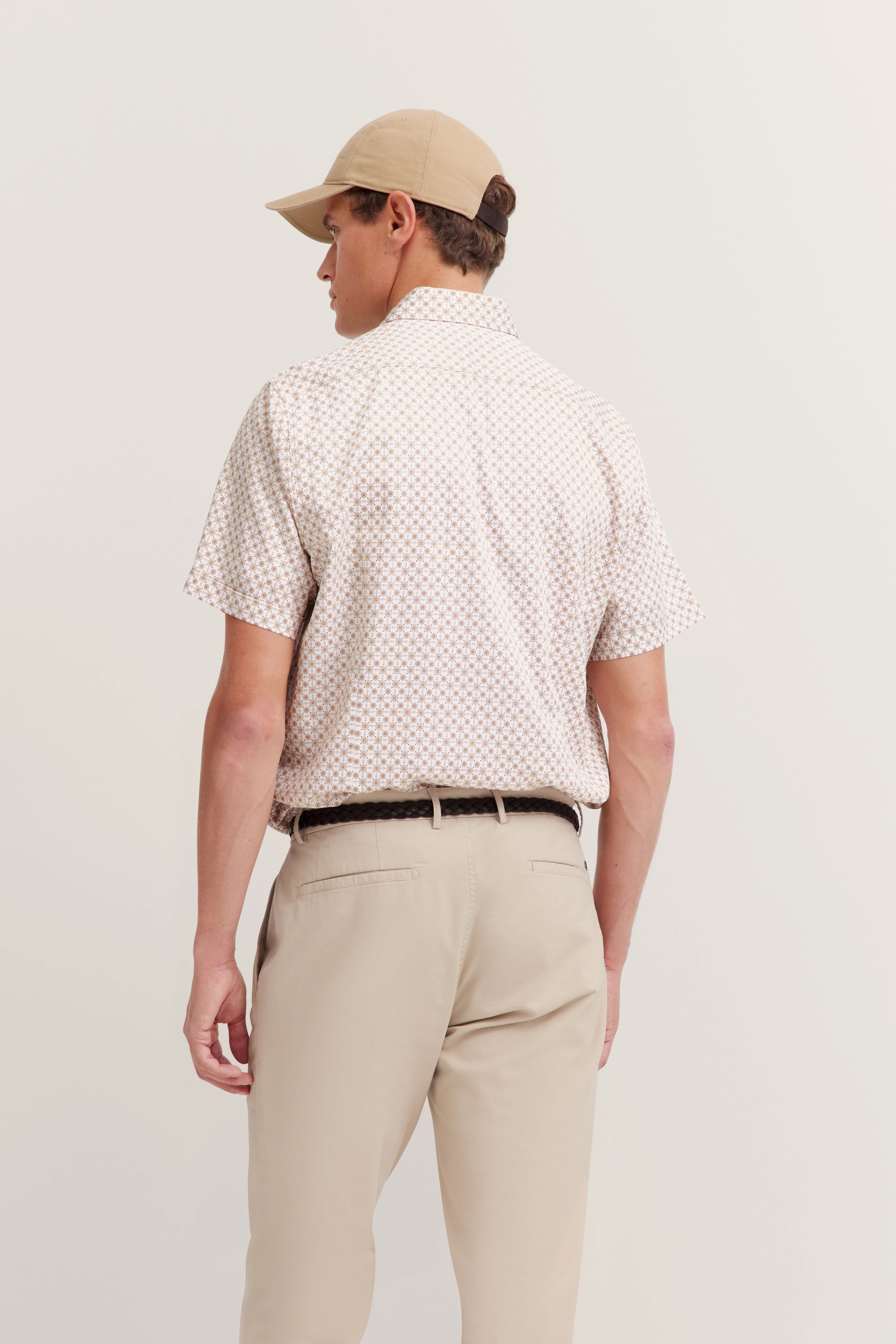 Model van achteren: Beige patroonhemd, lichte chino's, beige pet.