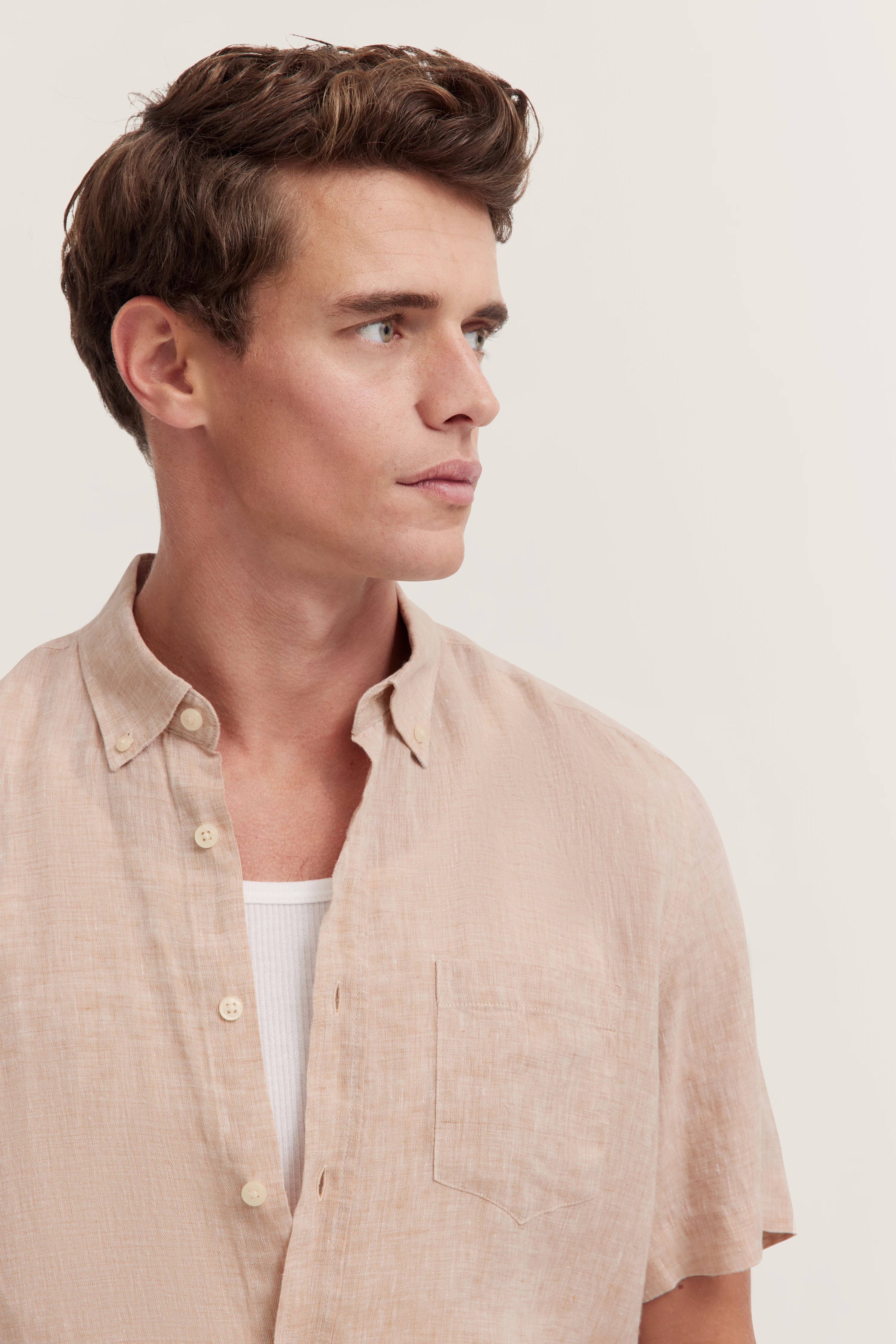 Beiges Kurzarmhemd über weißem Shirt, Model seitlich blickend, legeres Posing, bugatti Stil.