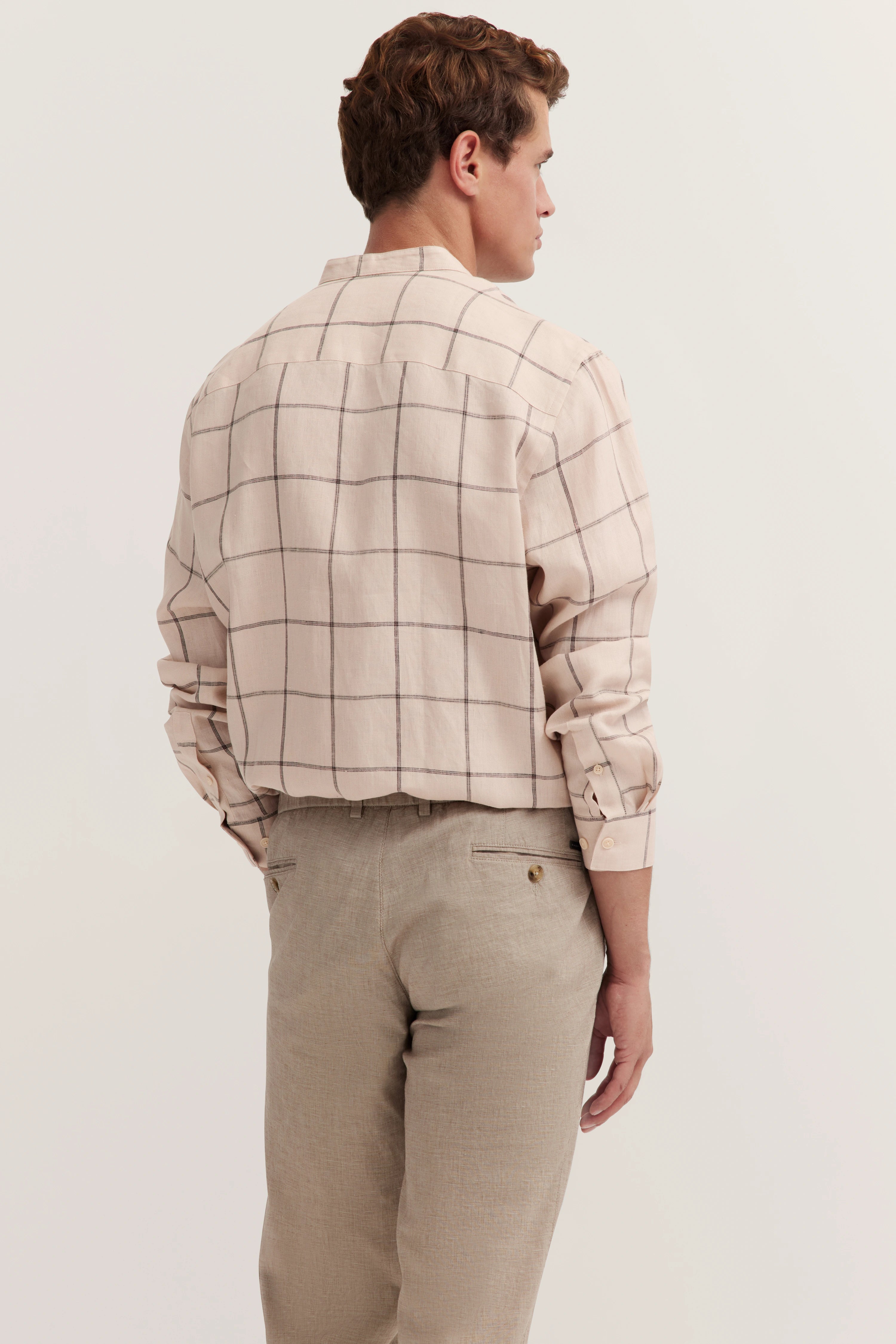Beigefarbene karierte bugatti Hemdbluse, beige Hose, Model von hinten, lässige Haltung.