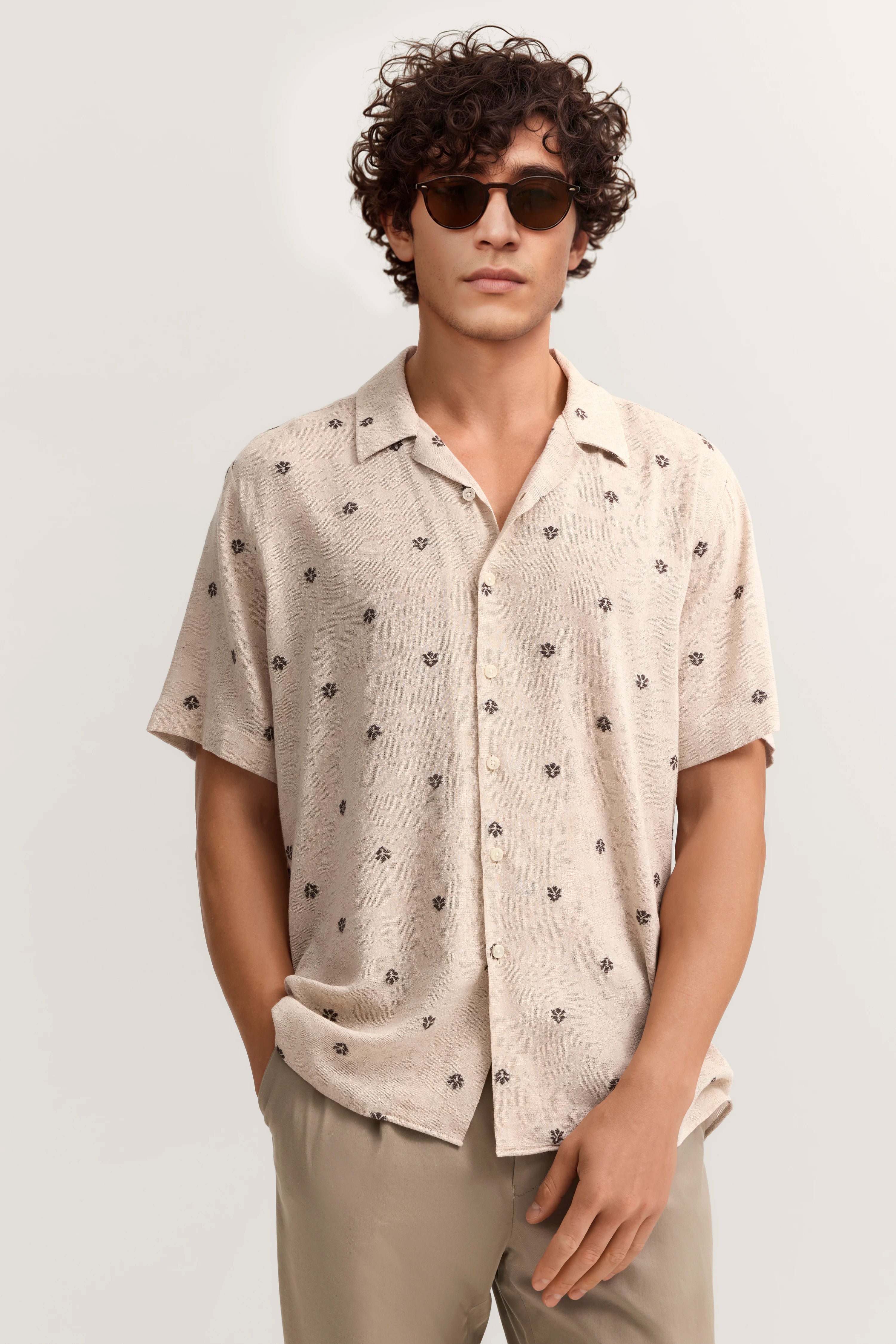 Beiges Hemd mit Blumenmuster, kurze Ärmel, lässig offen, Model in entspannter Pose, bugatti Stil.