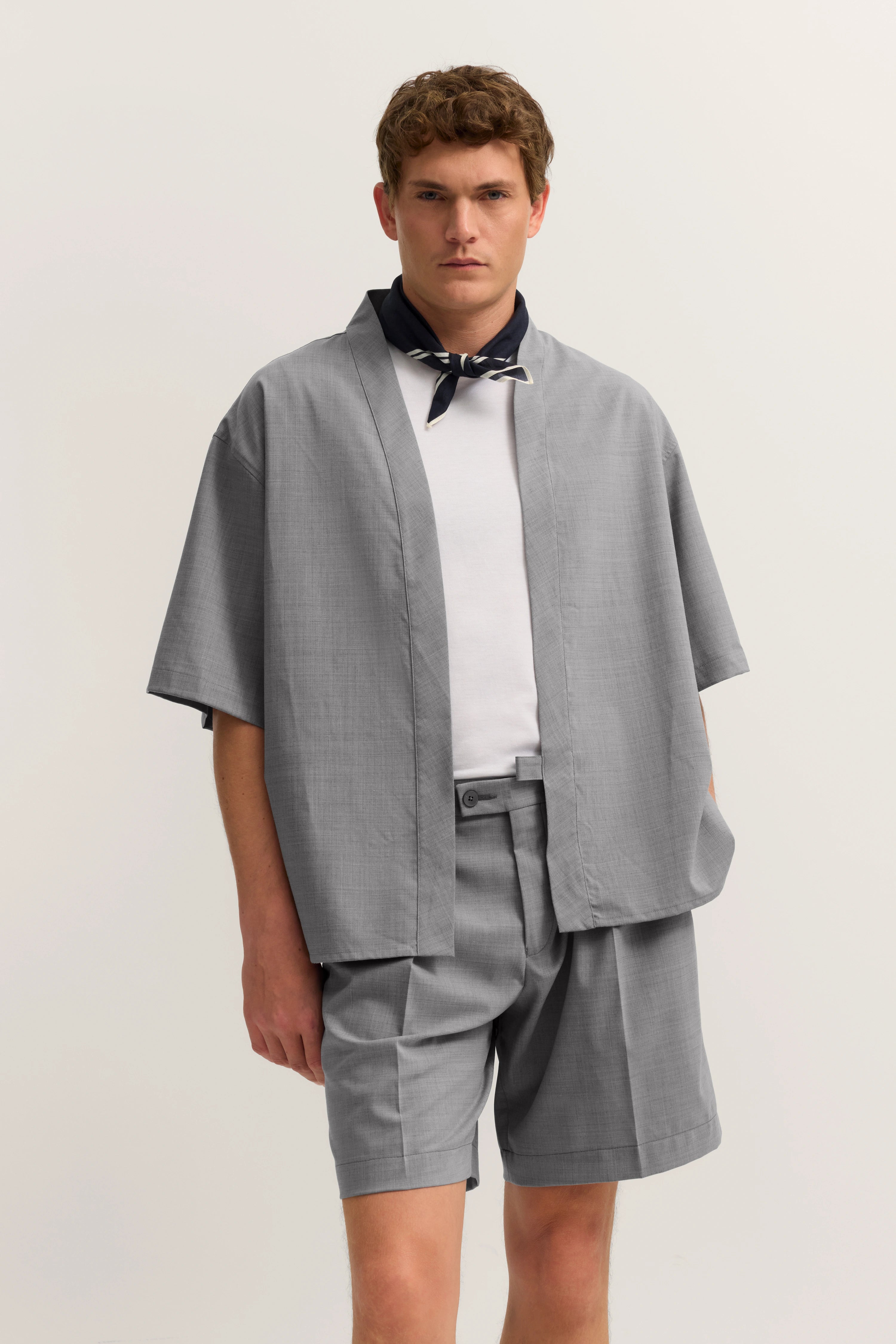 Graues bugatti Outfit mit Shorts und Kimono, weißes Shirt, schwarzes Halstuch, legeres Modelbild.