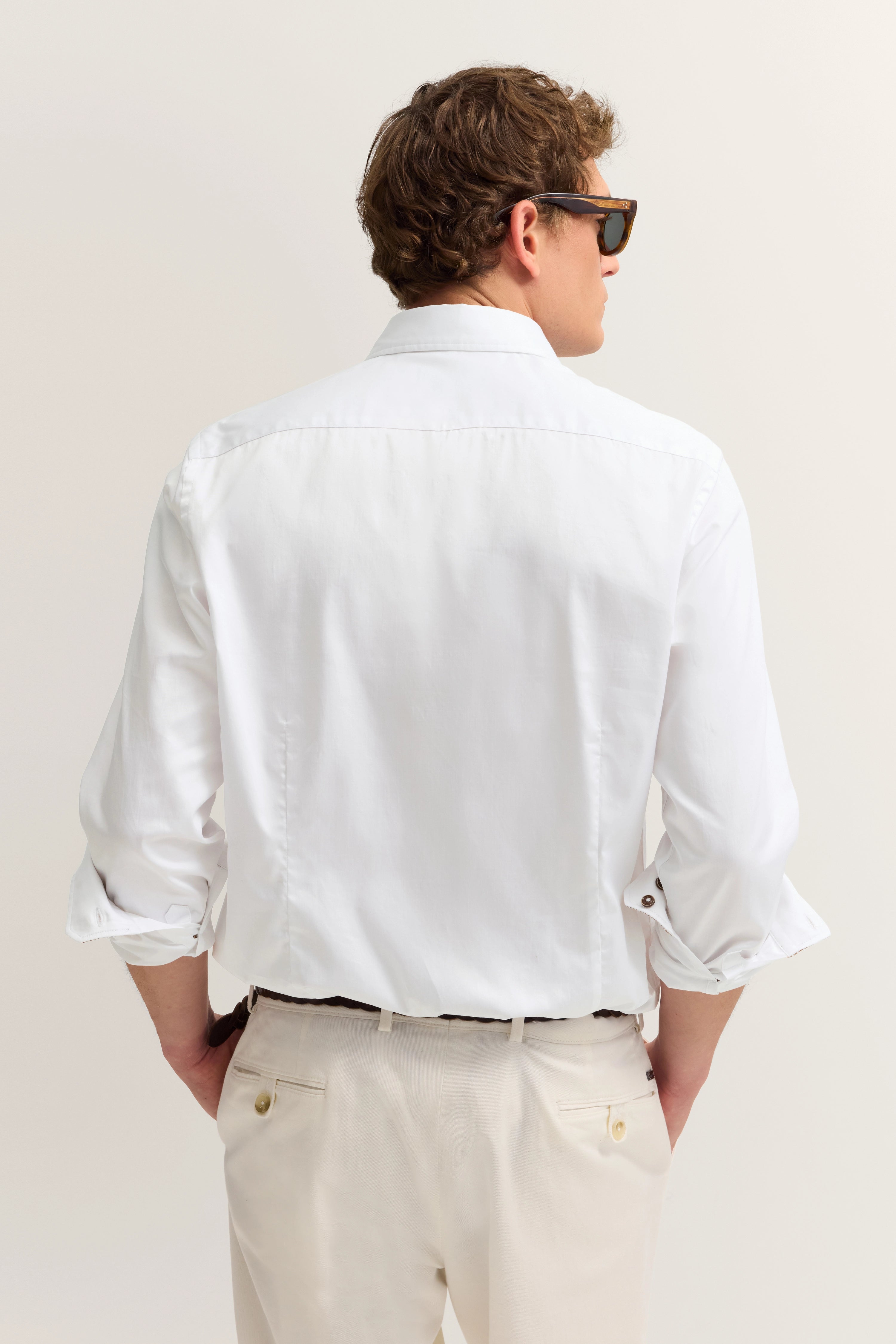 Weißes Hemd und beige Hose, Rückansicht, Modell mit Sonnenbrille, Hände in Hosentaschen.