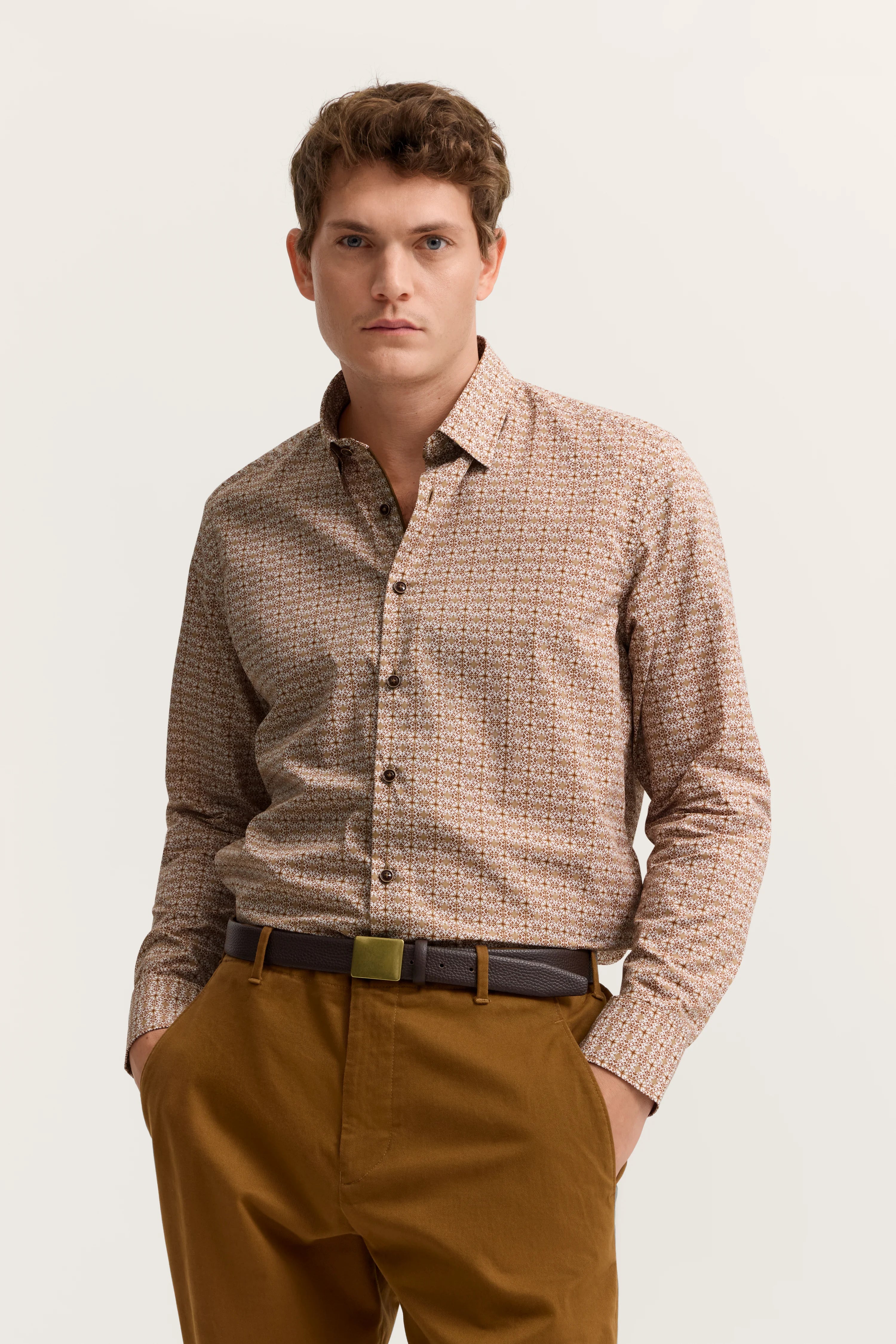 Braunes gemustertes Hemd mit brauner Hose, Modelbild, lässige Pose, Hände in den Taschen.