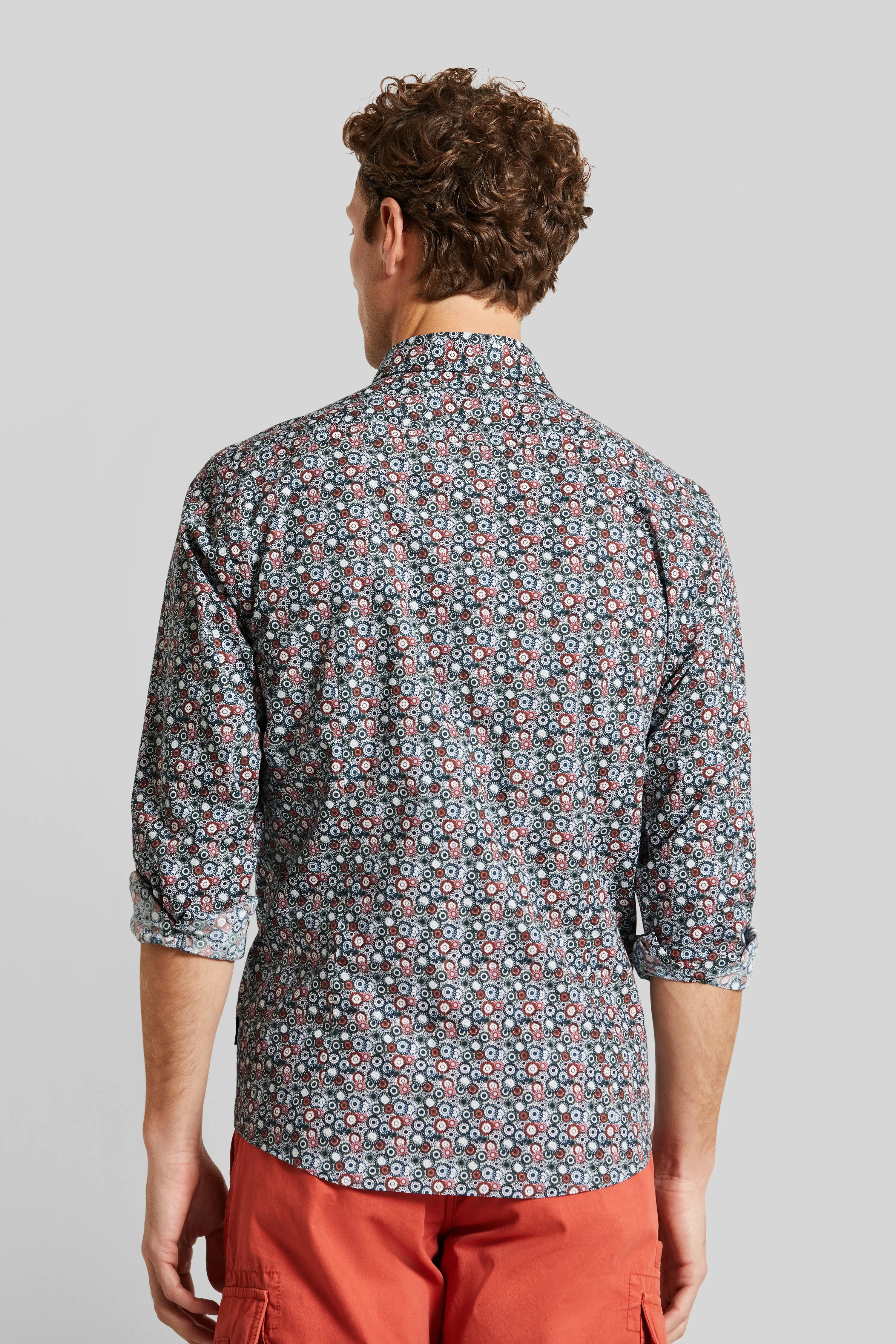 Rückansicht: Model trägt gemustertes Hemd in Blau-Rot mit hochgekrempelten Ärmeln und roten Shorts.