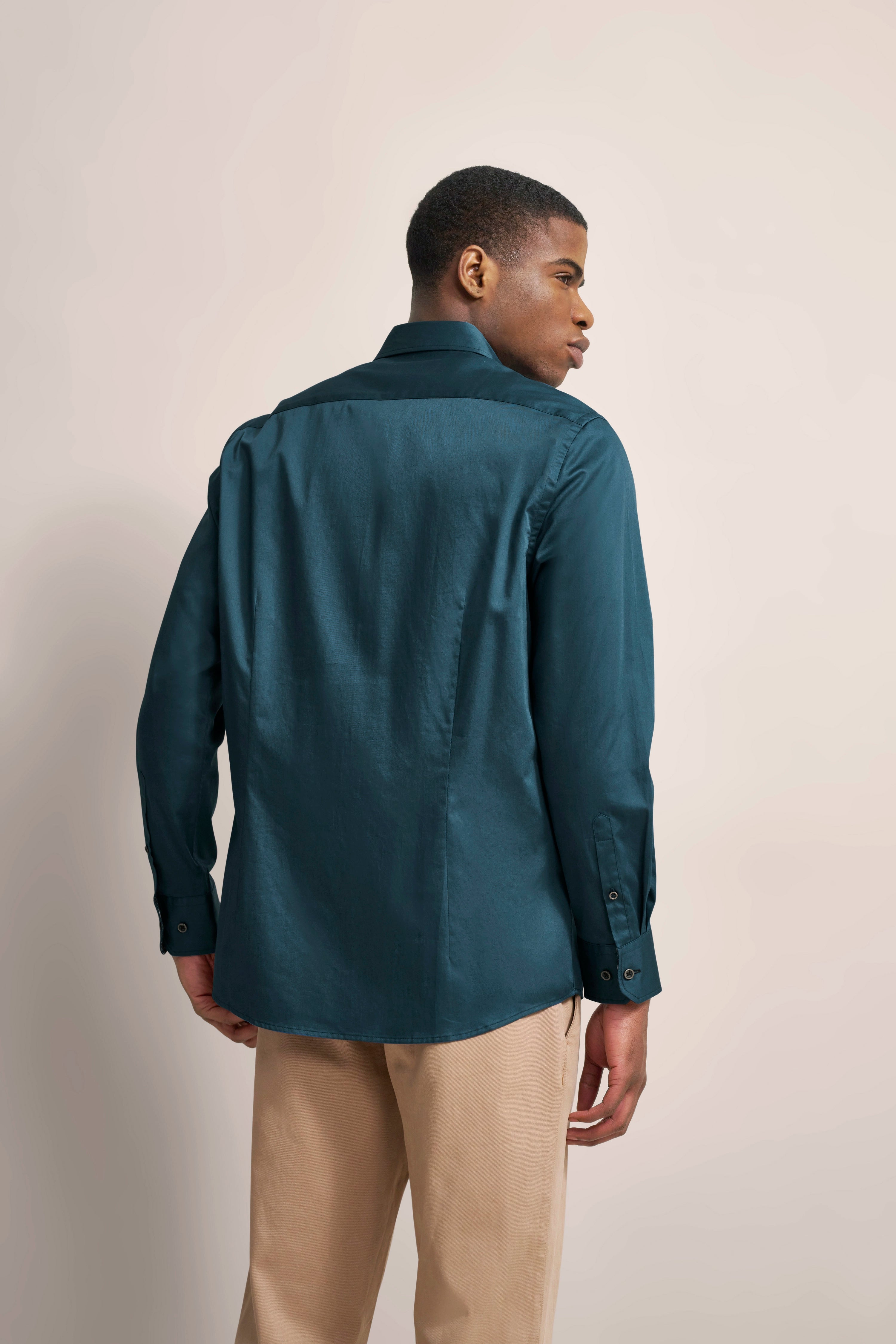 Model in teal bugatti Hemd und beige Hose, Rückansicht, legeres Posing.