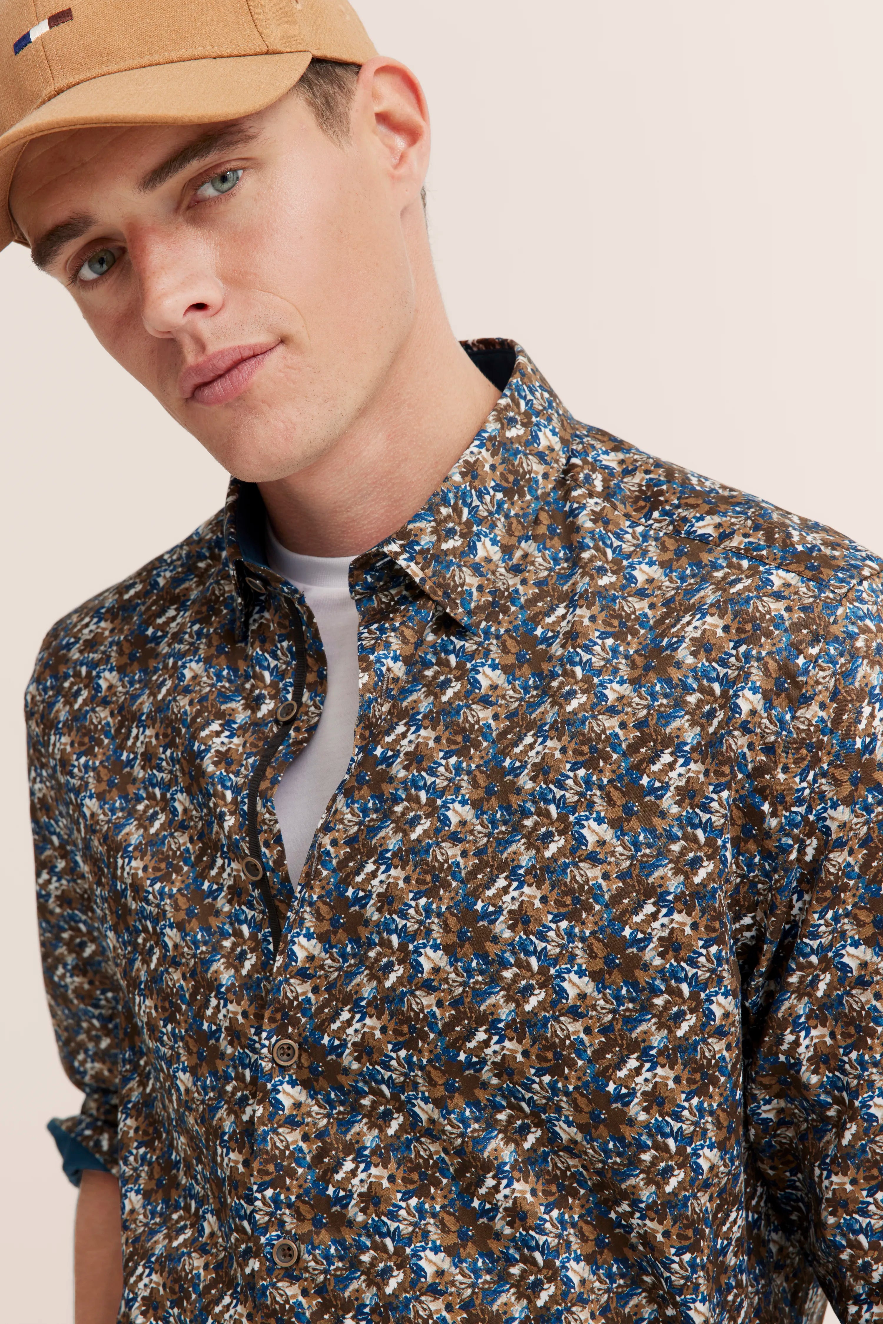 Model wearing brown-blue floral shirt by bugatti, casual pose with cap.