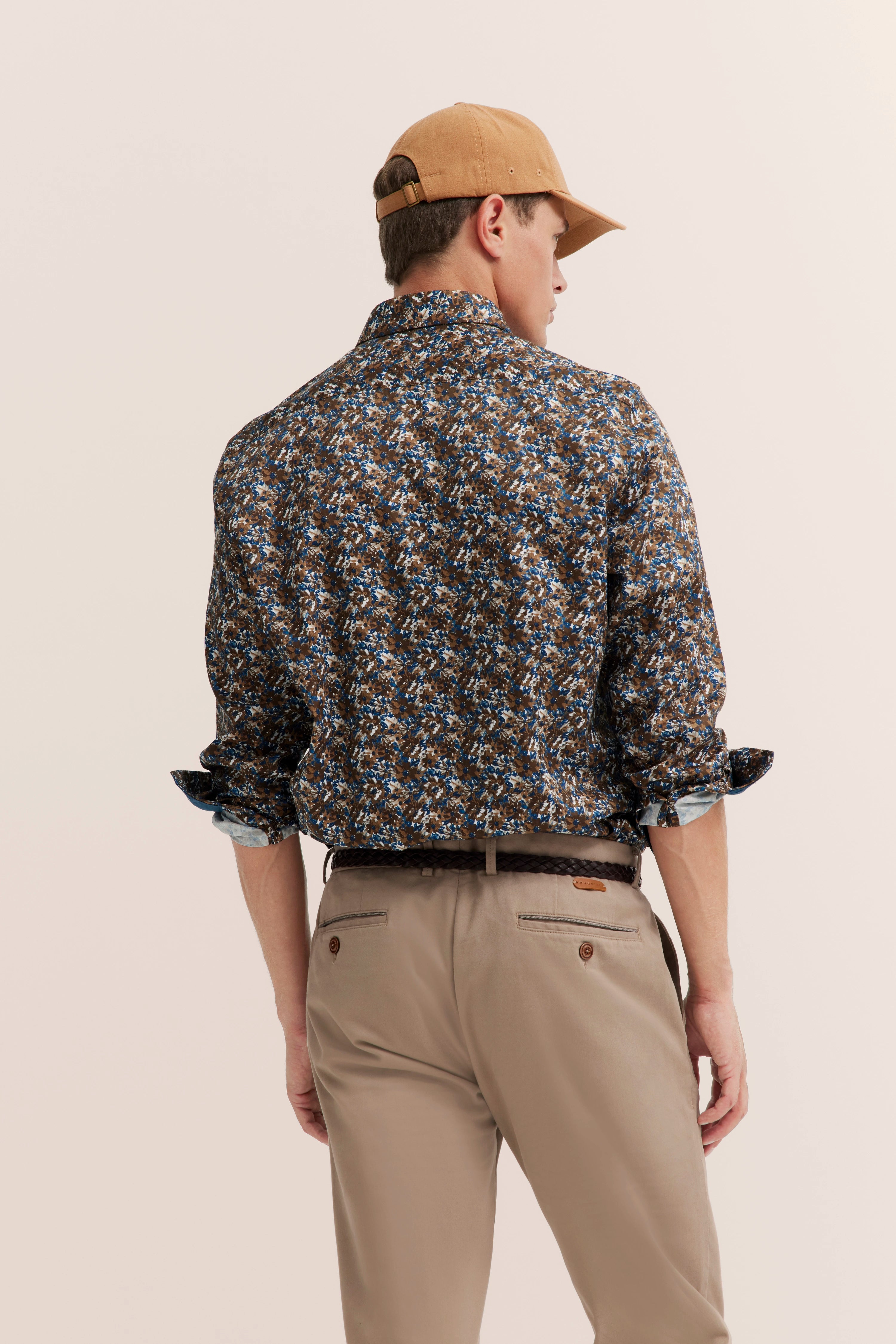 Man in patterned shirt, beige pants, brown cap, side pose, exuding bugatti's timeless style and Italian elegance.