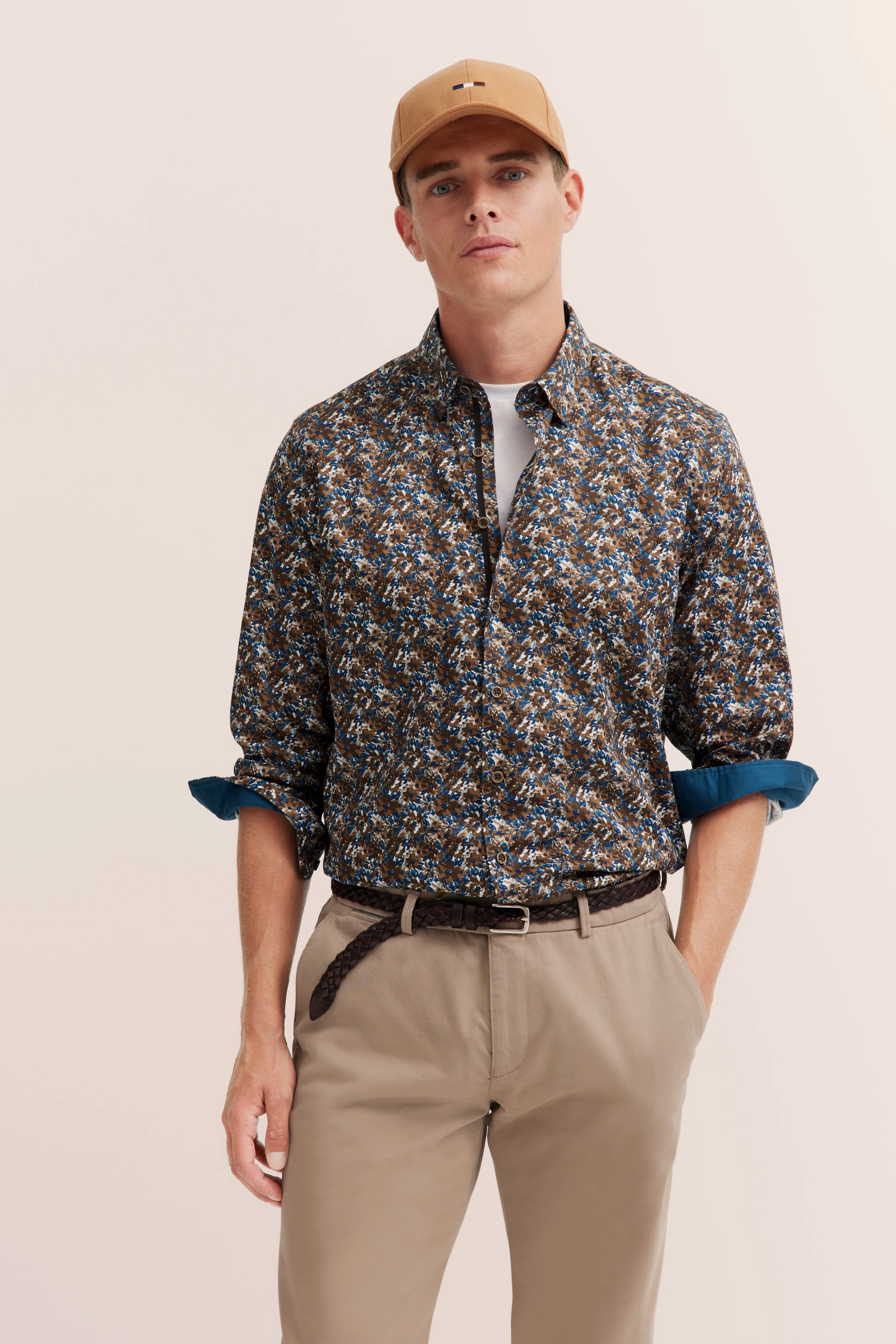 Herrenoutfit mit braunem, floralem Hemd und beiger Hose, Model posiert lässig, bugatti Stil.