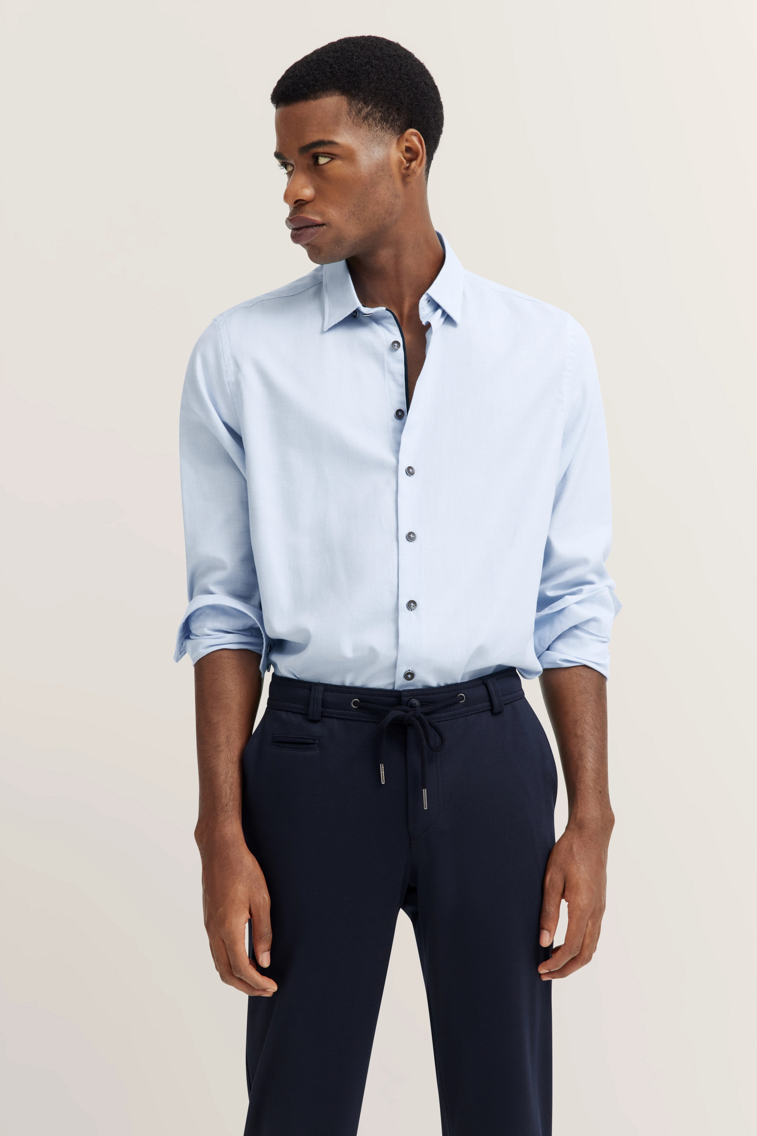 Model wears light blue shirt and dark blue pants by bugatti, casual pose, side view.